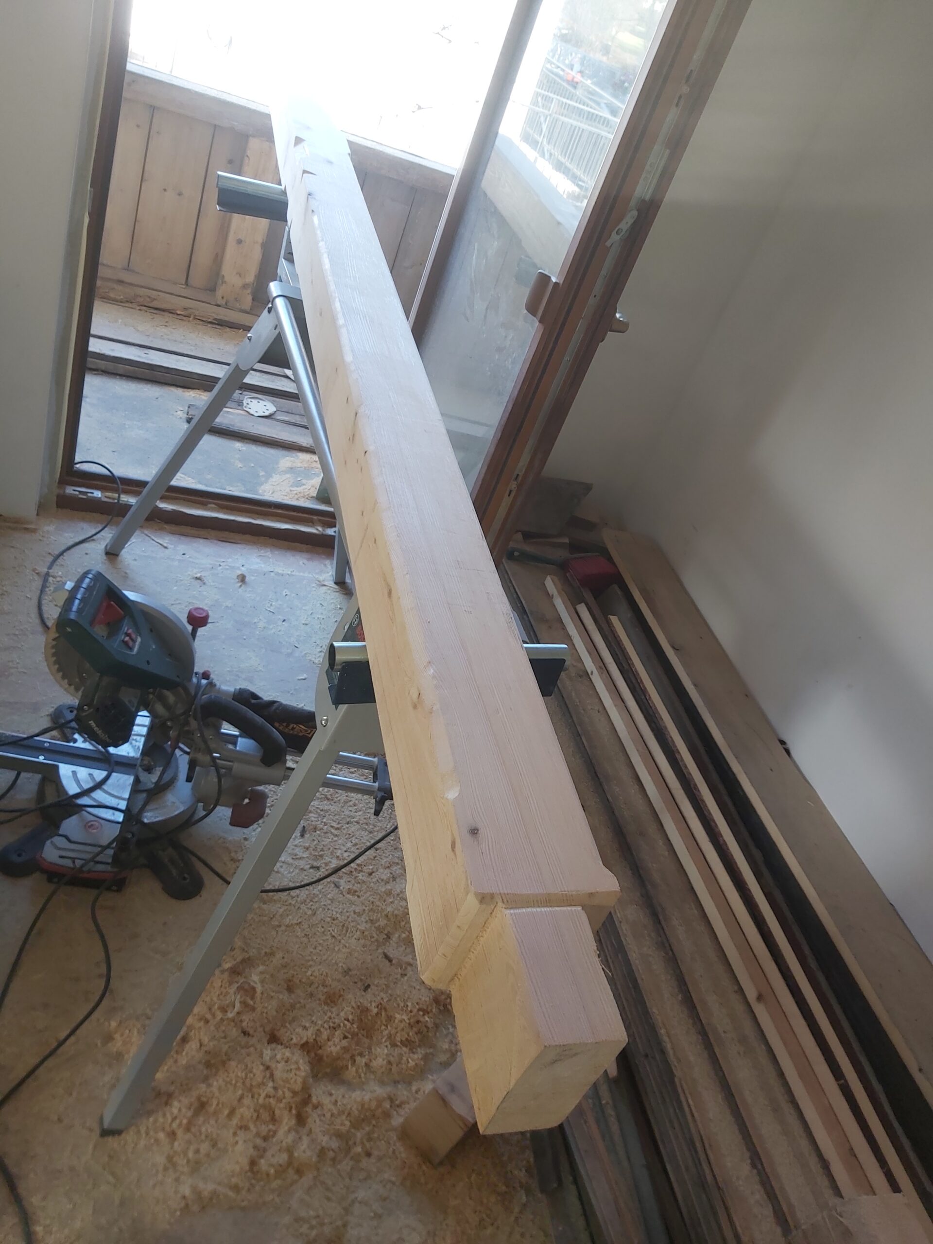 Drewniana belka obrabiana i przygotowywana do montażu, ułożona na kozłach roboczych w trakcie prac stolarskich we wnętrzu.