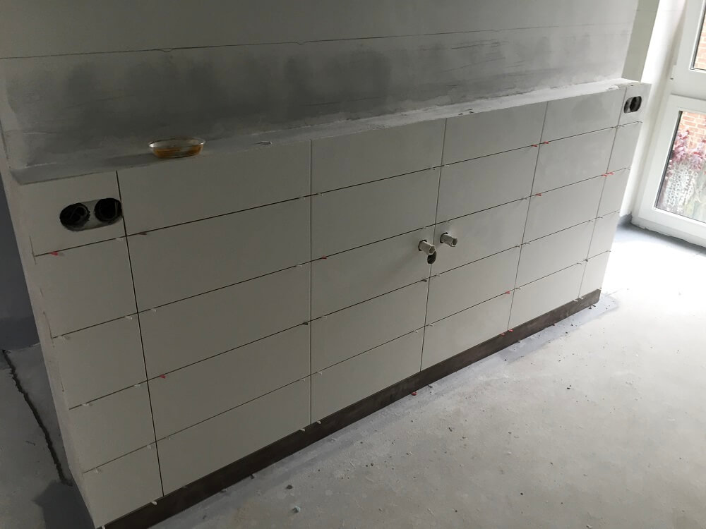 Białe płytki ścienne ułożone pod instalacje wodne i elektryczne, widok na etap prac wykończeniowych przed montażem wyposażenia.