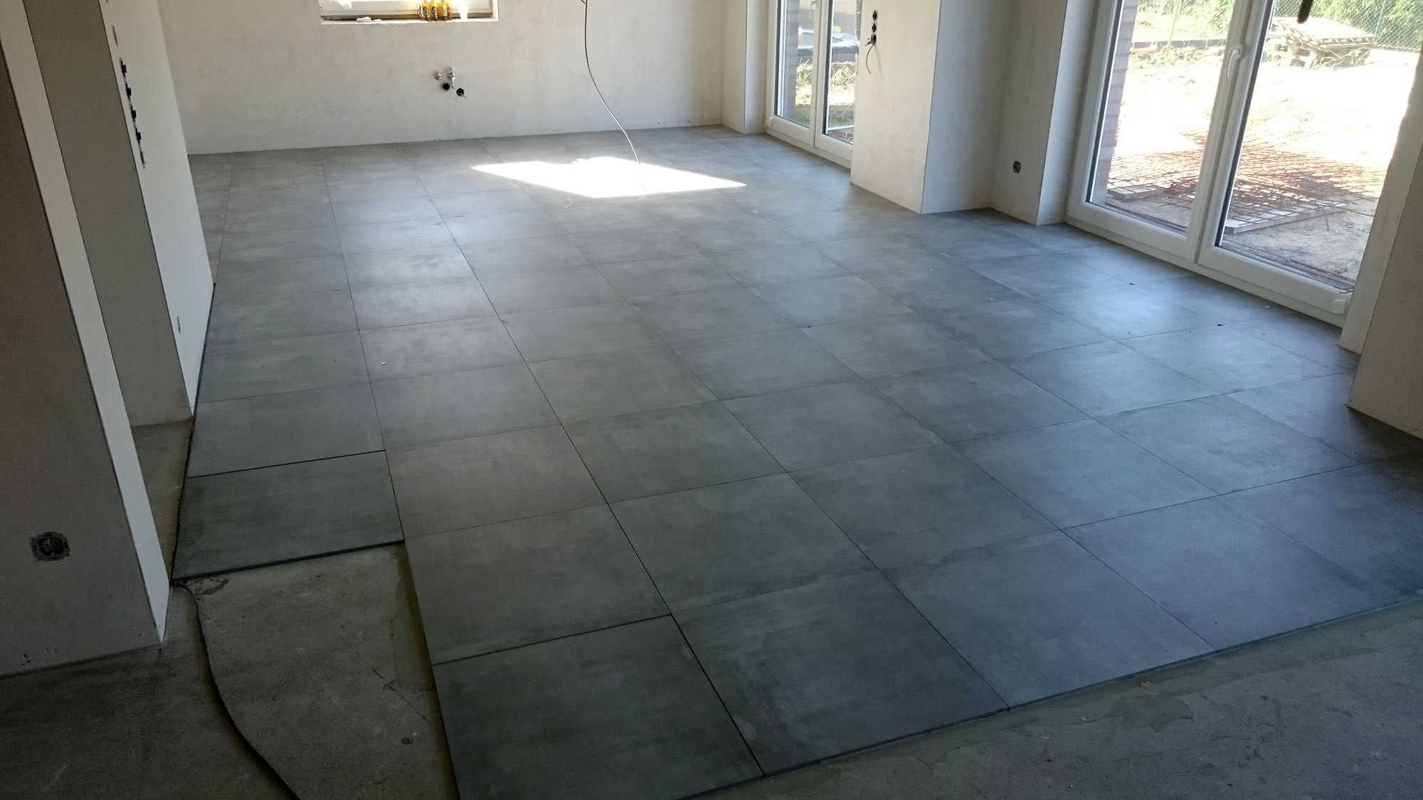 Szare płytki podłogowe ułożone w salonie, widok na gotową posadzkę przed dalszymi pracami wykończeniowymi.