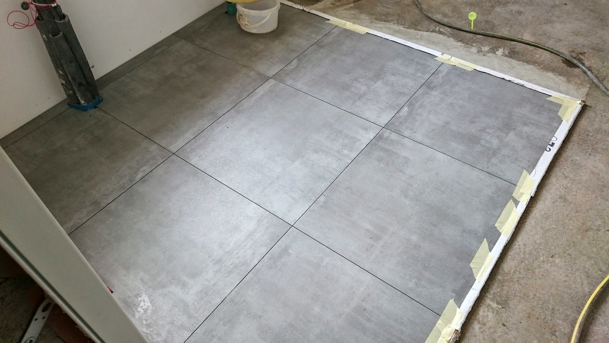 Szare płytki podłogowe ułożone w łazience, widok świeżo wykonanej posadzki w trakcie prac wykończeniowych.