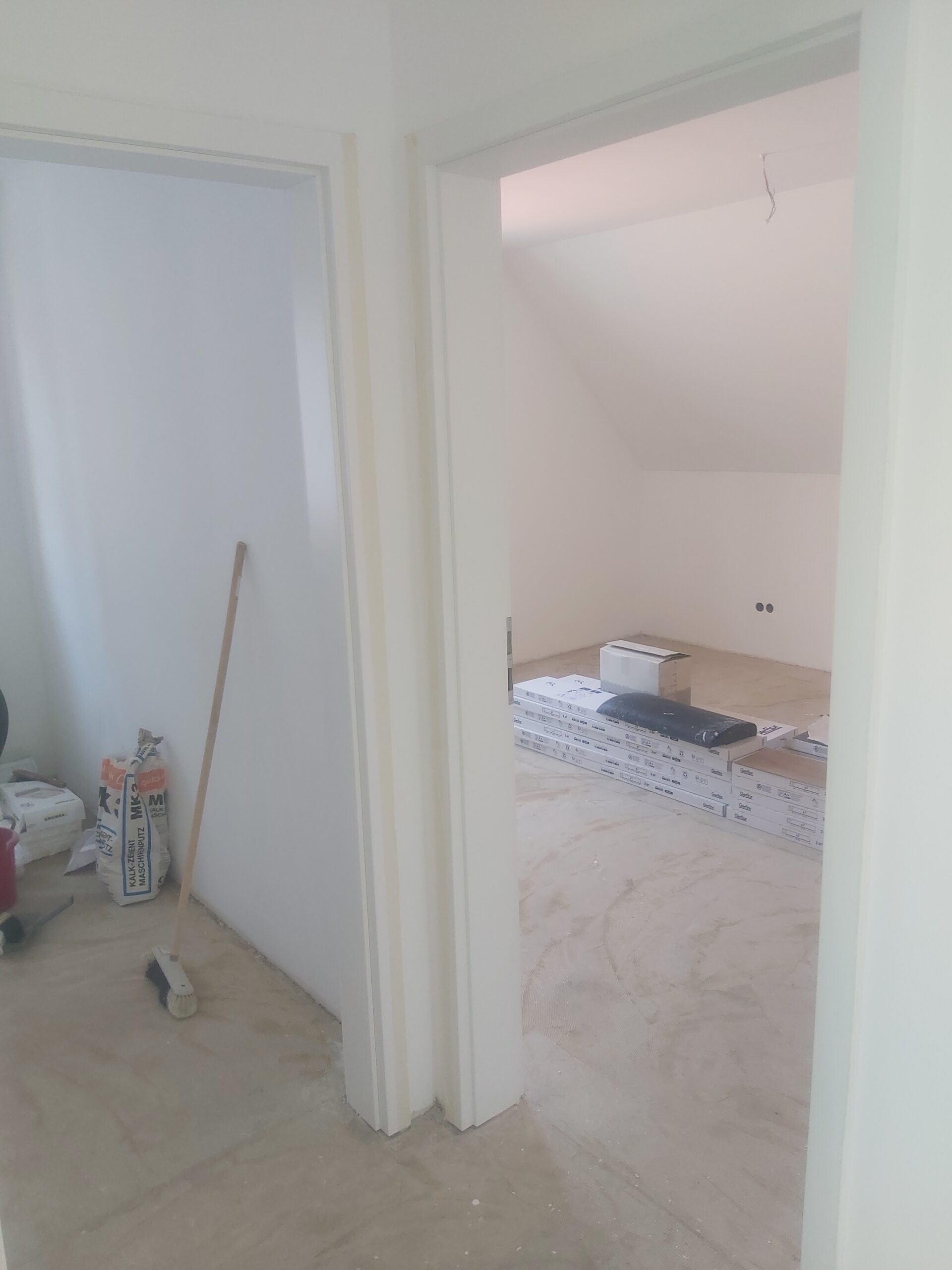 Widok na dwa sąsiadujące pomieszczenia w trakcie prac wykończeniowych, z widocznymi ościeżnicami drzwi, materiałami budowlanymi na podłodze oraz przygotowanymi ścianami do dalszych etapów remontu.
