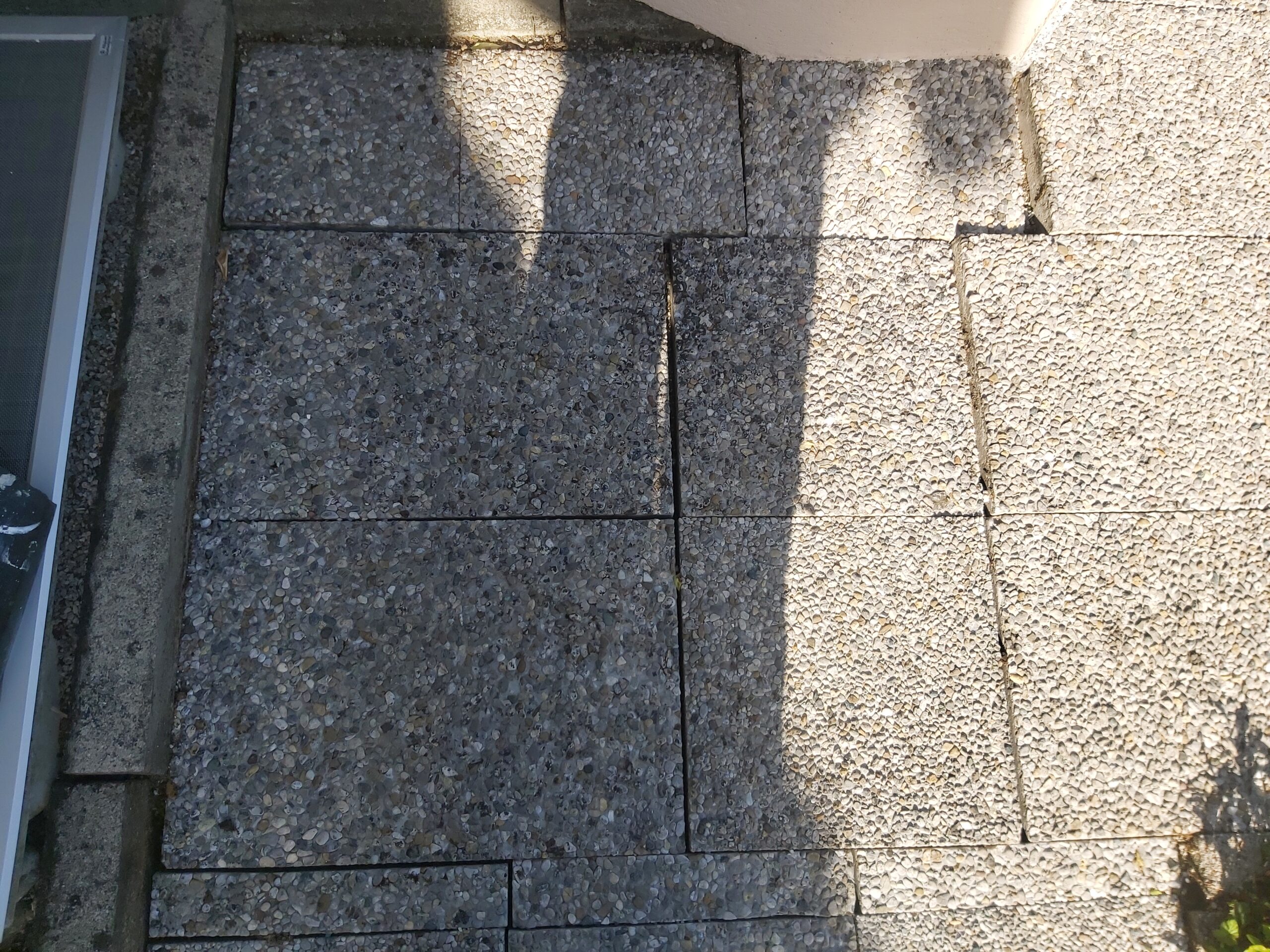 Widok z góry na fragment nawierzchni z kostki brukowej przy budynku, pokazujący dokładne dopasowanie elementów oraz równe linie cięć i fug.