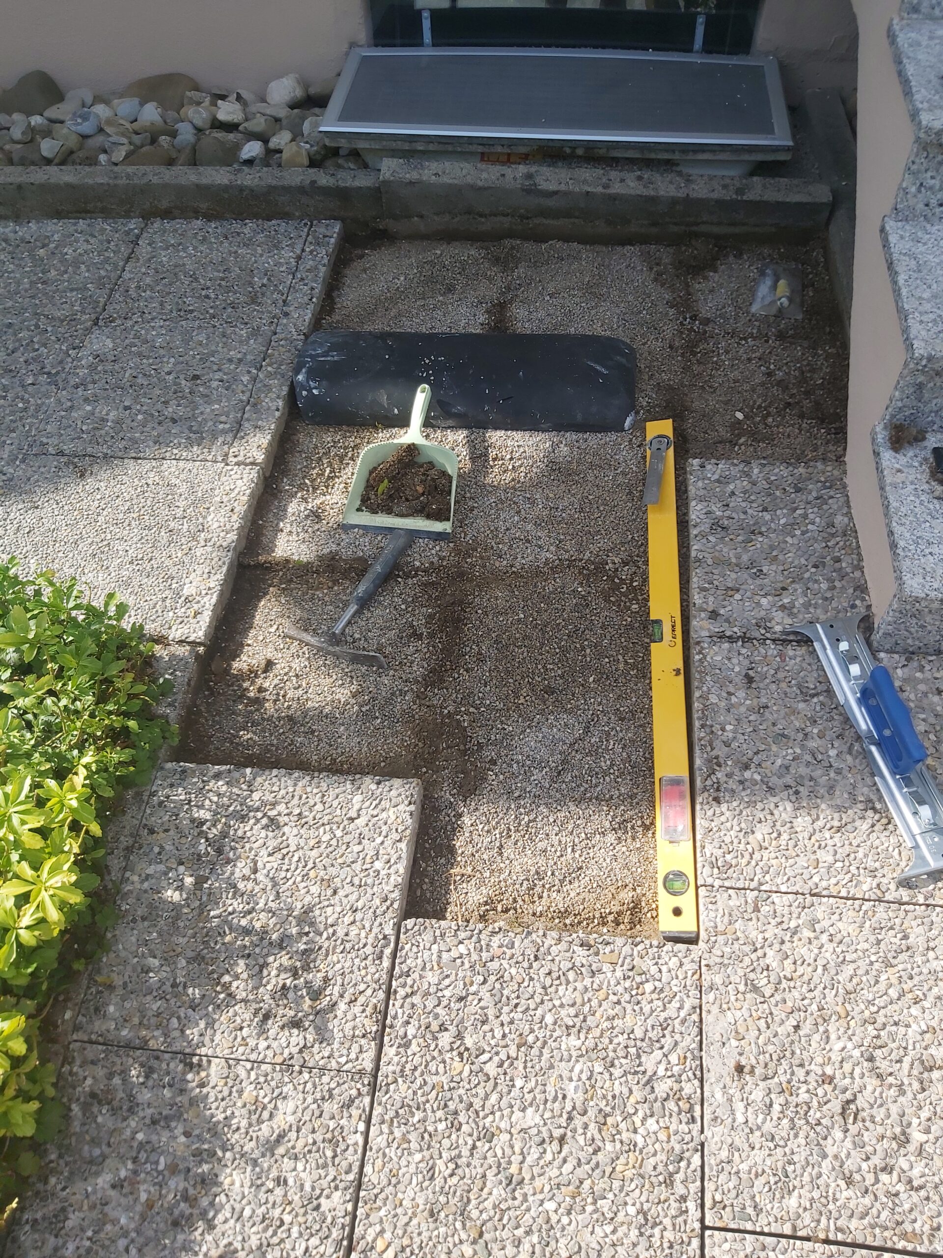 Wyrównane podłoże pod kostkę brukową przy budynku z widoczną poziomicą, szuflą i narzędziami używanymi podczas precyzyjnych prac brukarskich.