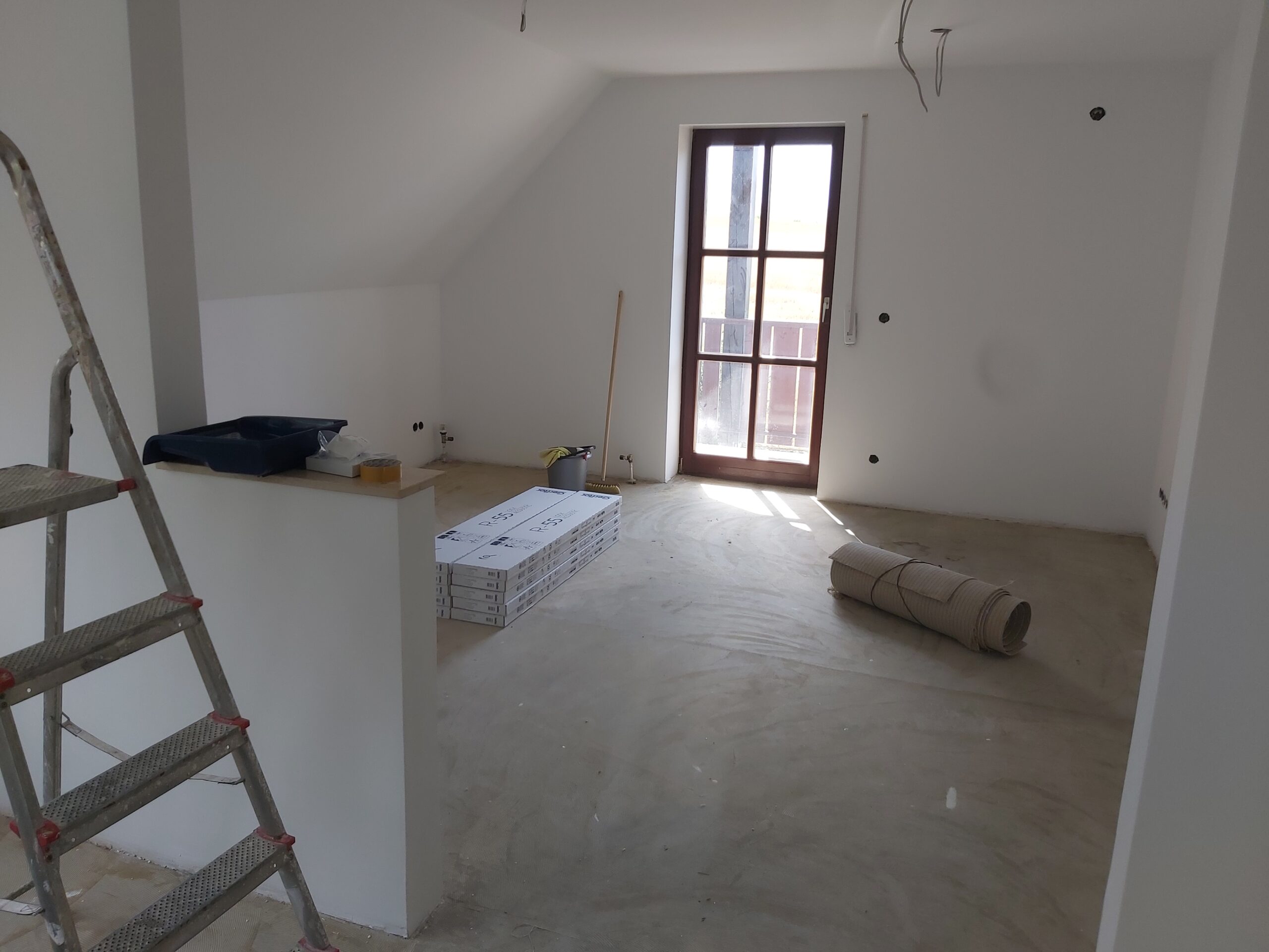 Pomieszczenie po remoncie w stanie wykończeniowym, z gładkimi ścianami, przygotowaną podłogą oraz drzwiami balkonowymi doświetlającymi wnętrze.