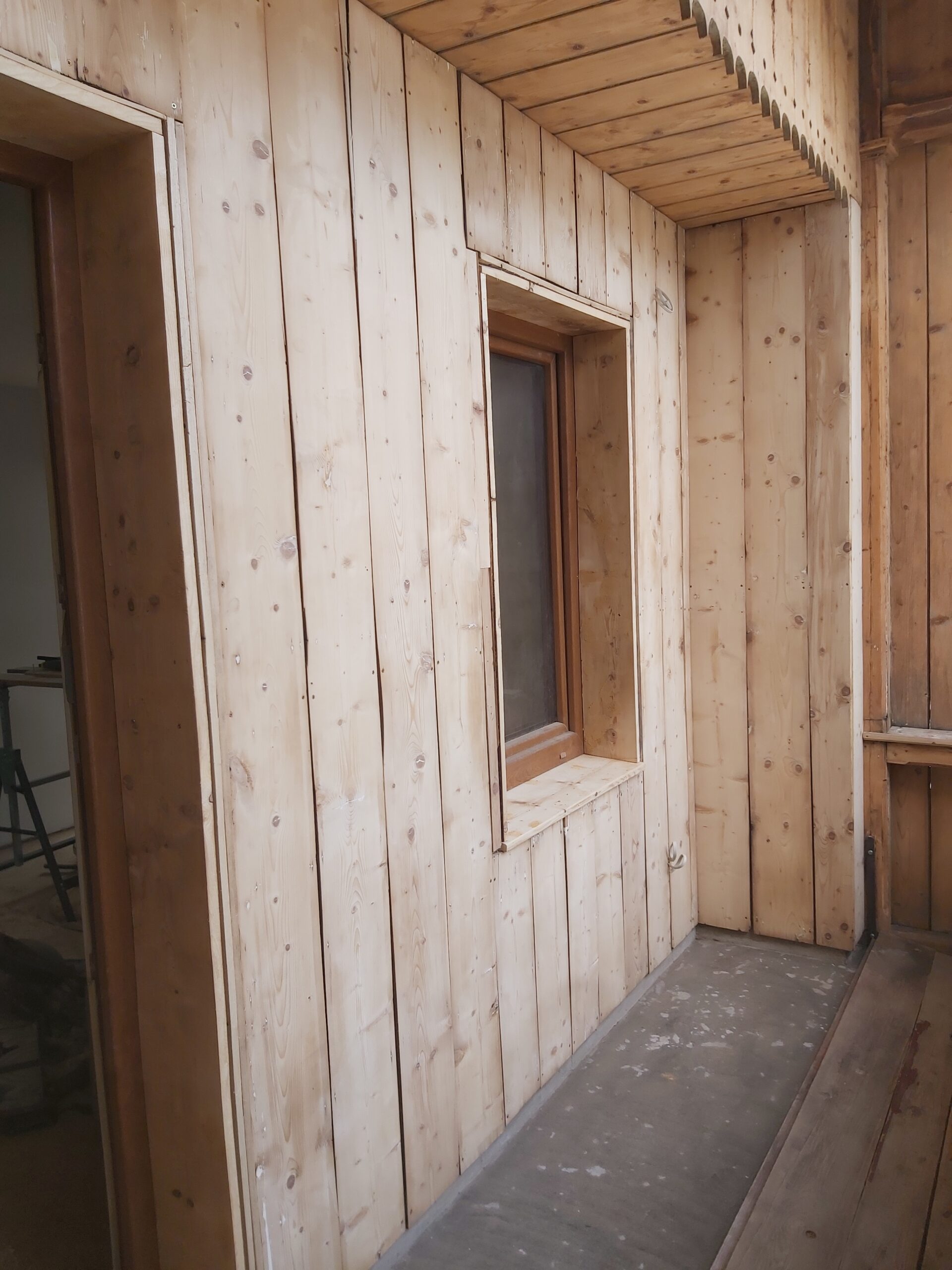 Drewniana zabudowa balkonu po remoncie, jasne deski ścienne, sufit z drewna oraz okno osadzone w nowej konstrukcji.