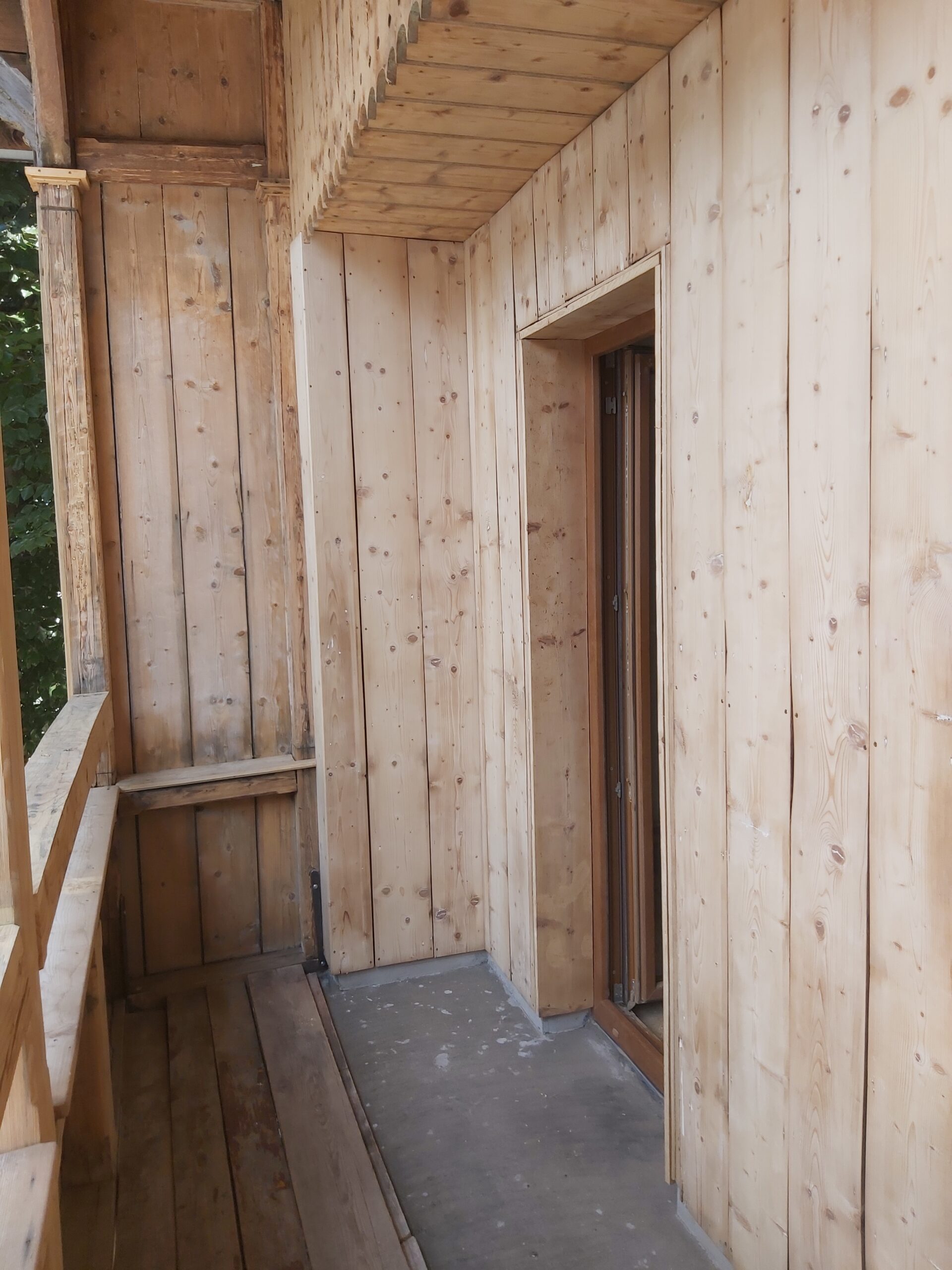 Drewniana zabudowa balkonu po remoncie, widoczne nowe deski ścienne, sufit oraz wejście do mieszkania.