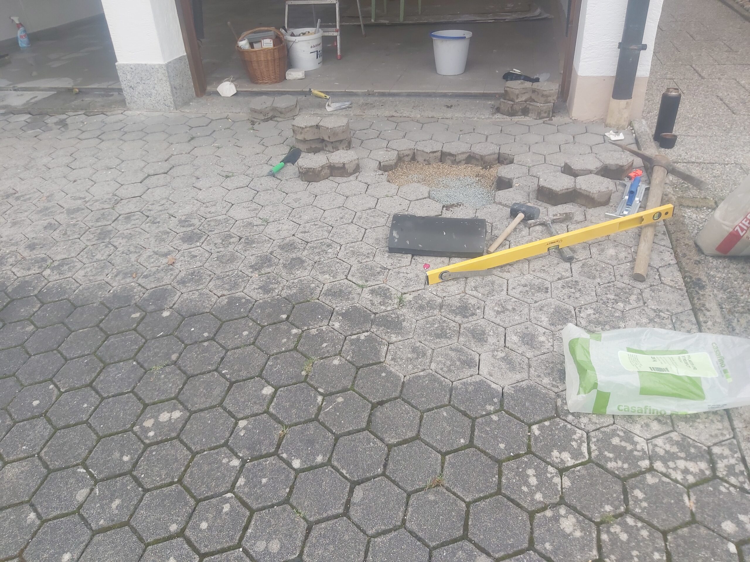 Fragment placu z kostki brukowej w trakcie naprawy, z usuniętymi elementami, widocznymi narzędziami brukarskimi i przygotowanym miejscem do uzupełnienia nawierzchni.