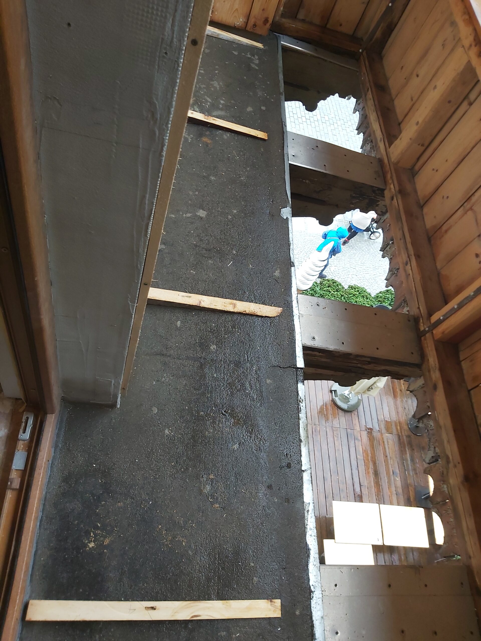 Widok z góry na balkon z odsłoniętą konstrukcją podłogi, widoczne belki nośne, warstwa izolacyjna oraz listwy dystansowe przed montażem płyt.