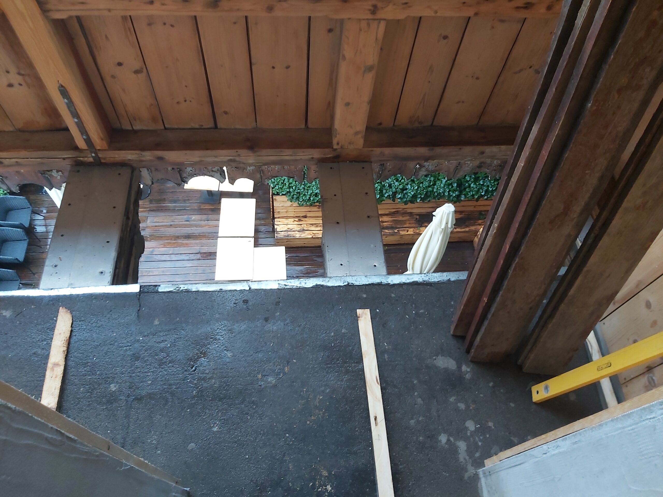 Widok od góry na odsłoniętą konstrukcję balkonu z belkami i pustą przestrzenią pod podłogą, etap przygotowania przed ułożeniem płyt OSB.