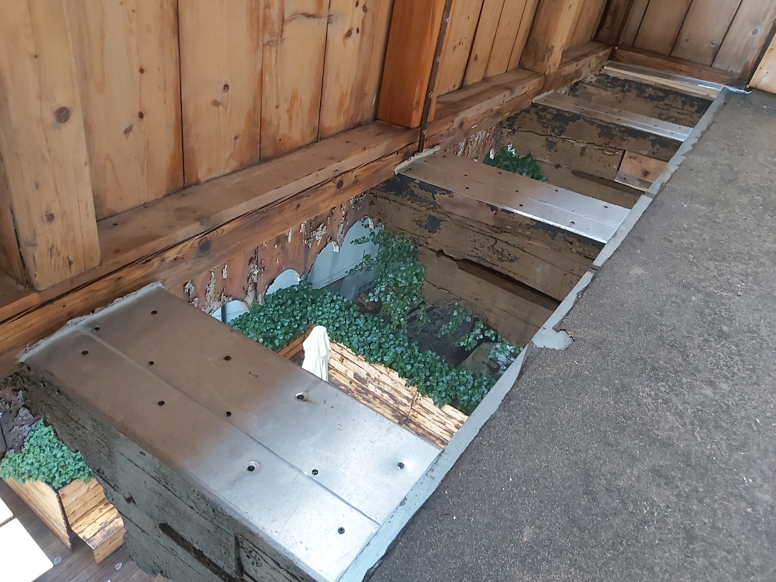 Odsłonięta konstrukcja balkonu z widocznymi legarami drewnianymi, metalowymi wzmocnieniami oraz zieloną warstwą izolacyjną pomiędzy belkami.