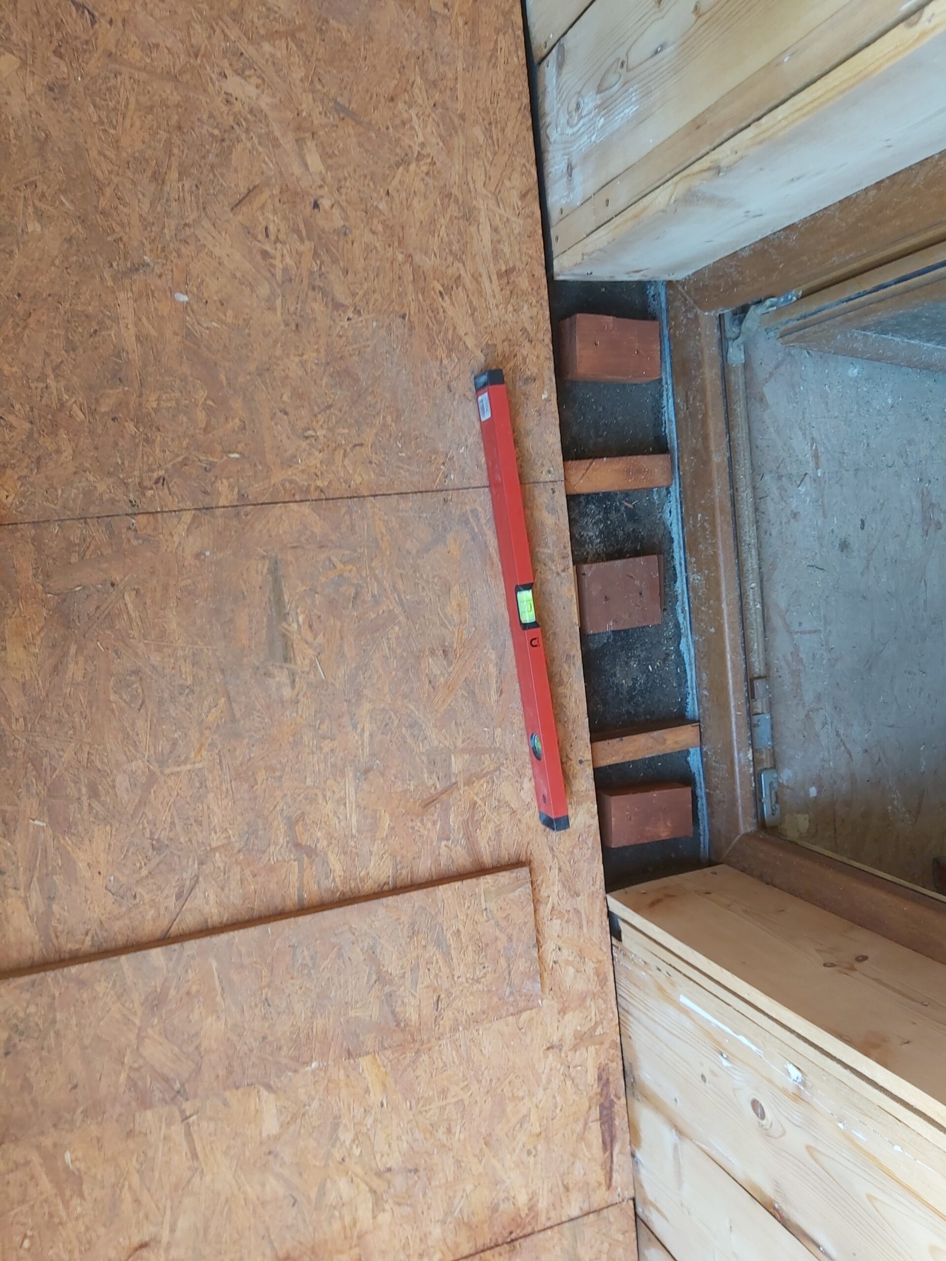 Płyty OSB na podłodze balkonu z widocznym progiem drzwiowym i poziomicą.