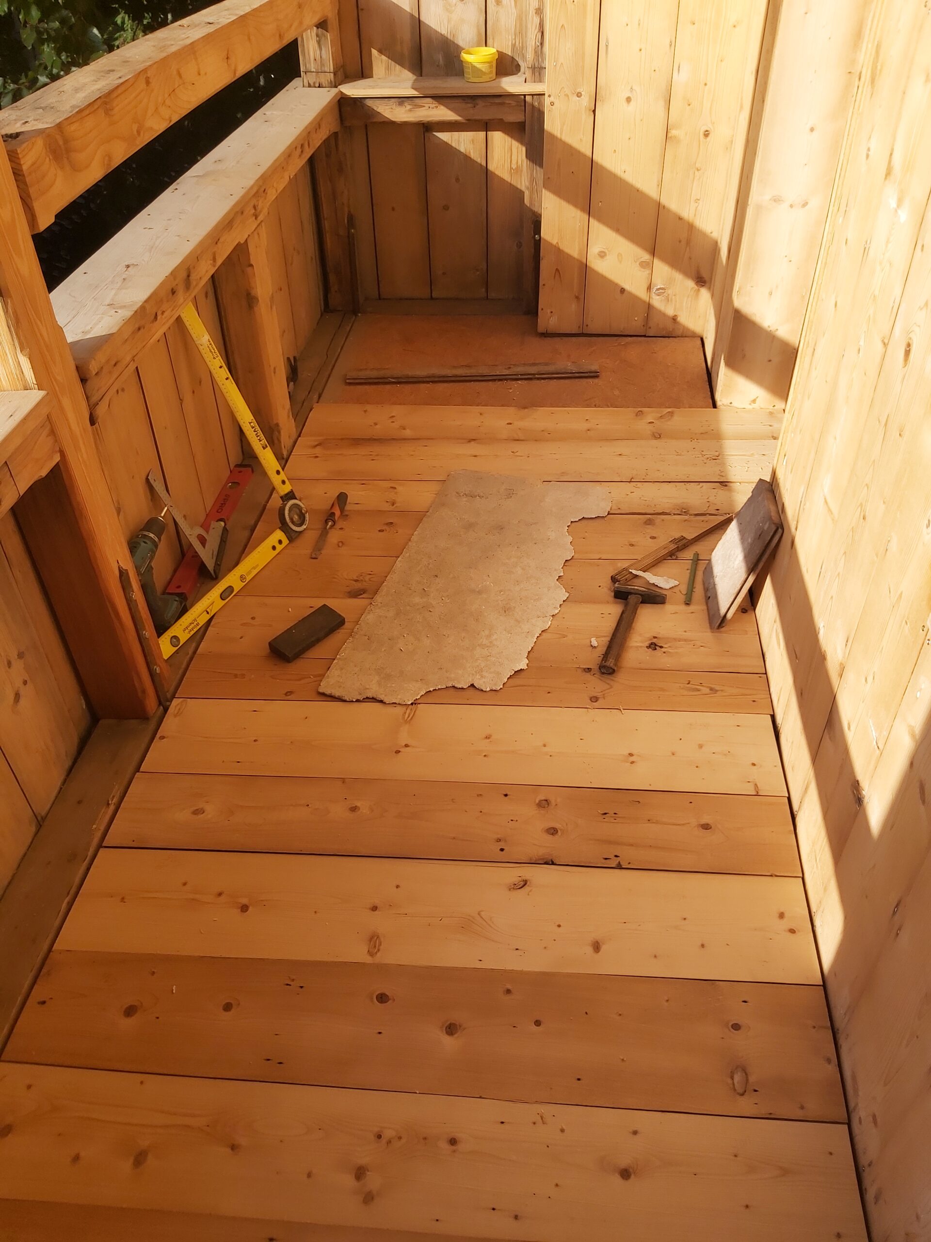 Drewniana podłoga na balkonie z ułożonych jasnych desek, na środku leżą narzędzia i fragment płyty podczas prac wykończeniowych.