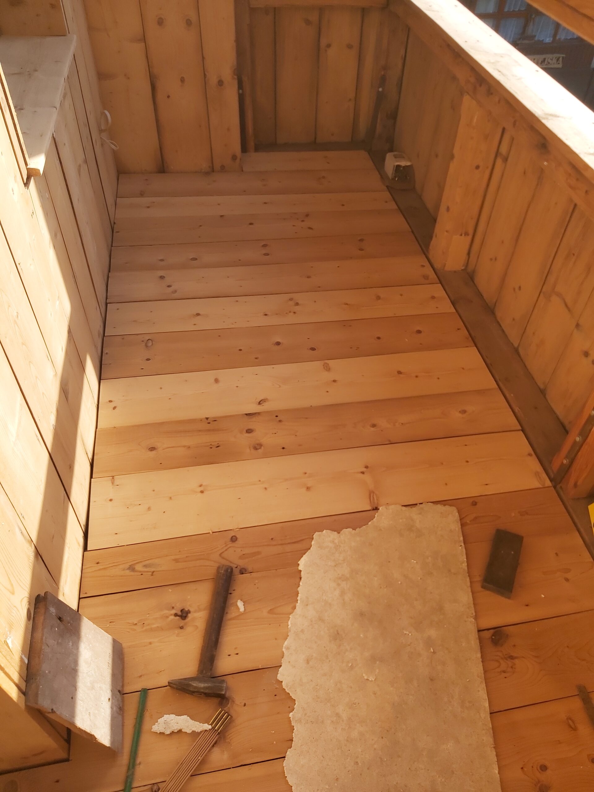 Nowa drewniana podłoga z jasnych desek na balkonie, widok z góry, fragment narzędzi i materiałów po pracach remontowych.