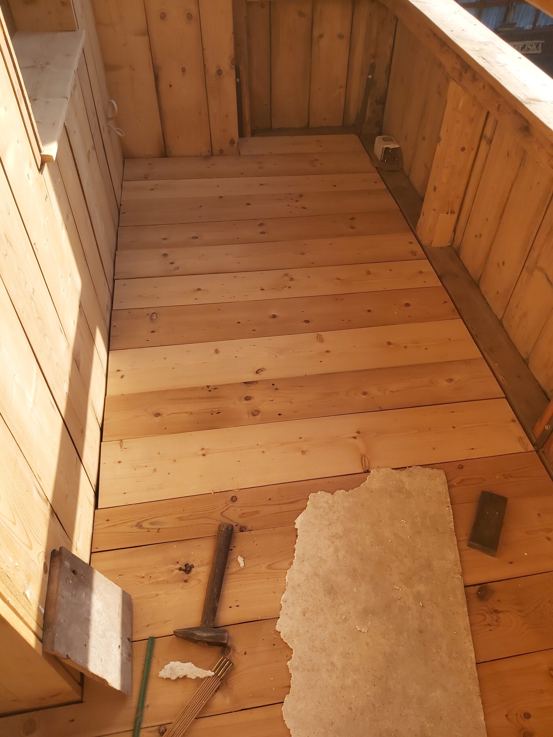 Jasna drewniana podłoga z desek na balkonie, widok z góry, fragment narzędzi i materiałów po zakończeniu prac wykończeniowych.