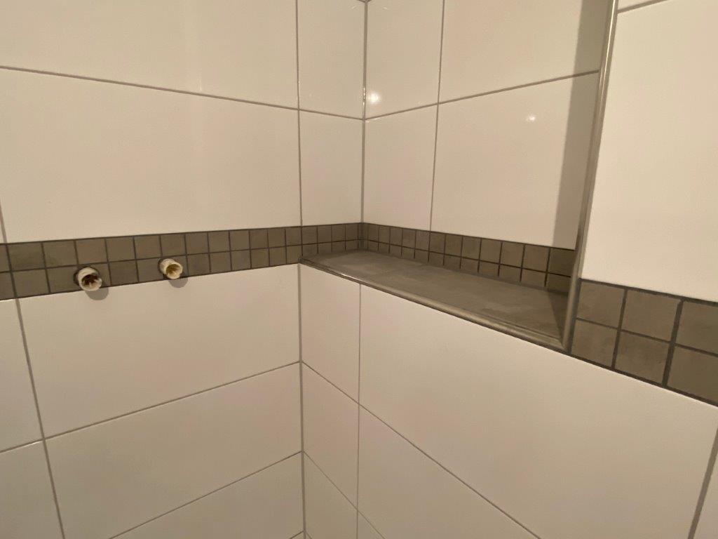 Wnęka prysznicowa z półką wykończoną płytkami, widoczne przyłącza instalacji wodnej w ścianie.