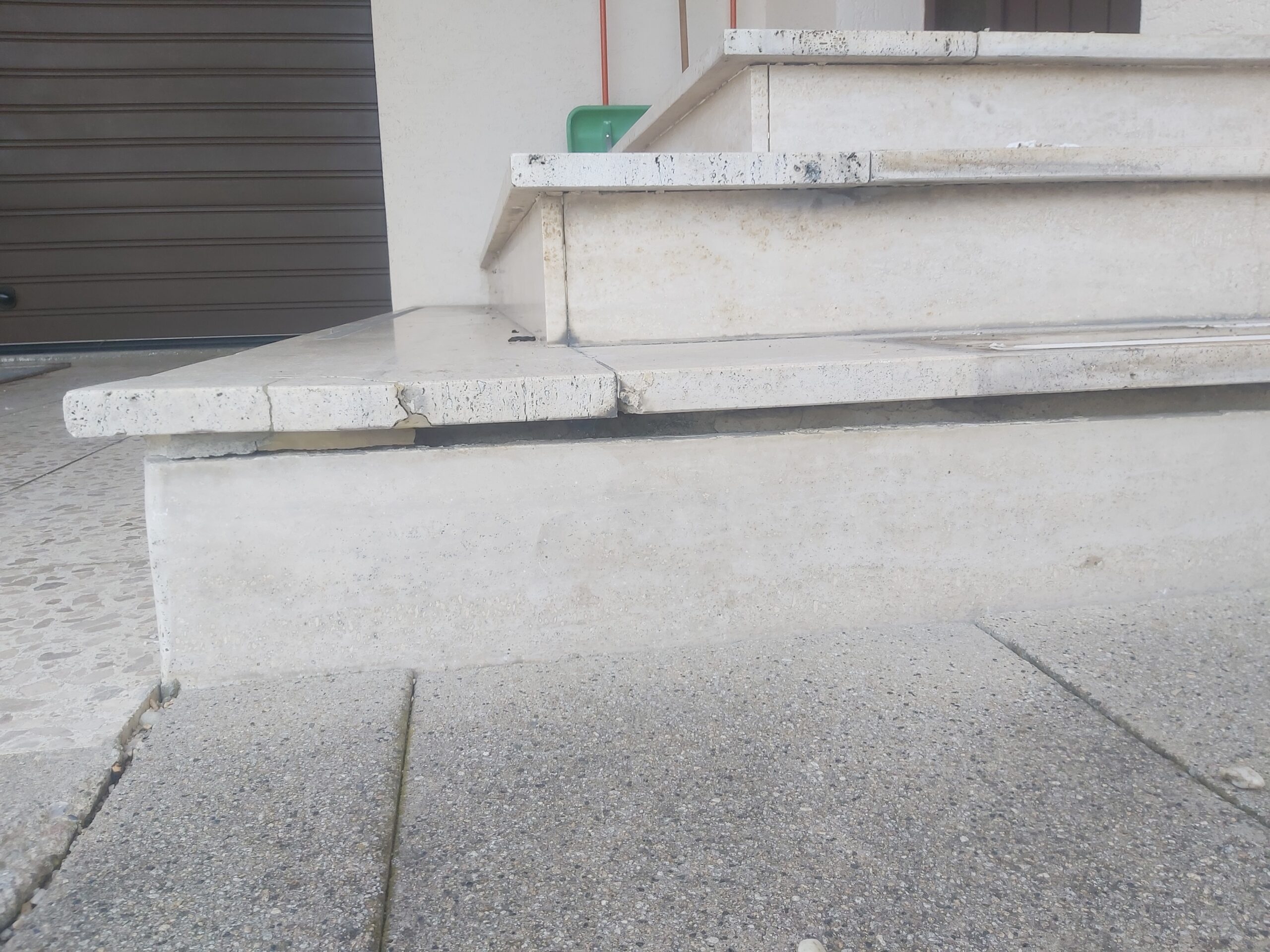 Widok na schody wejściowe z kamiennymi stopniami, widoczne pęknięcia i ubytki materiału na krawędziach oraz ślady zabrudzeń eksploatacyjnych.