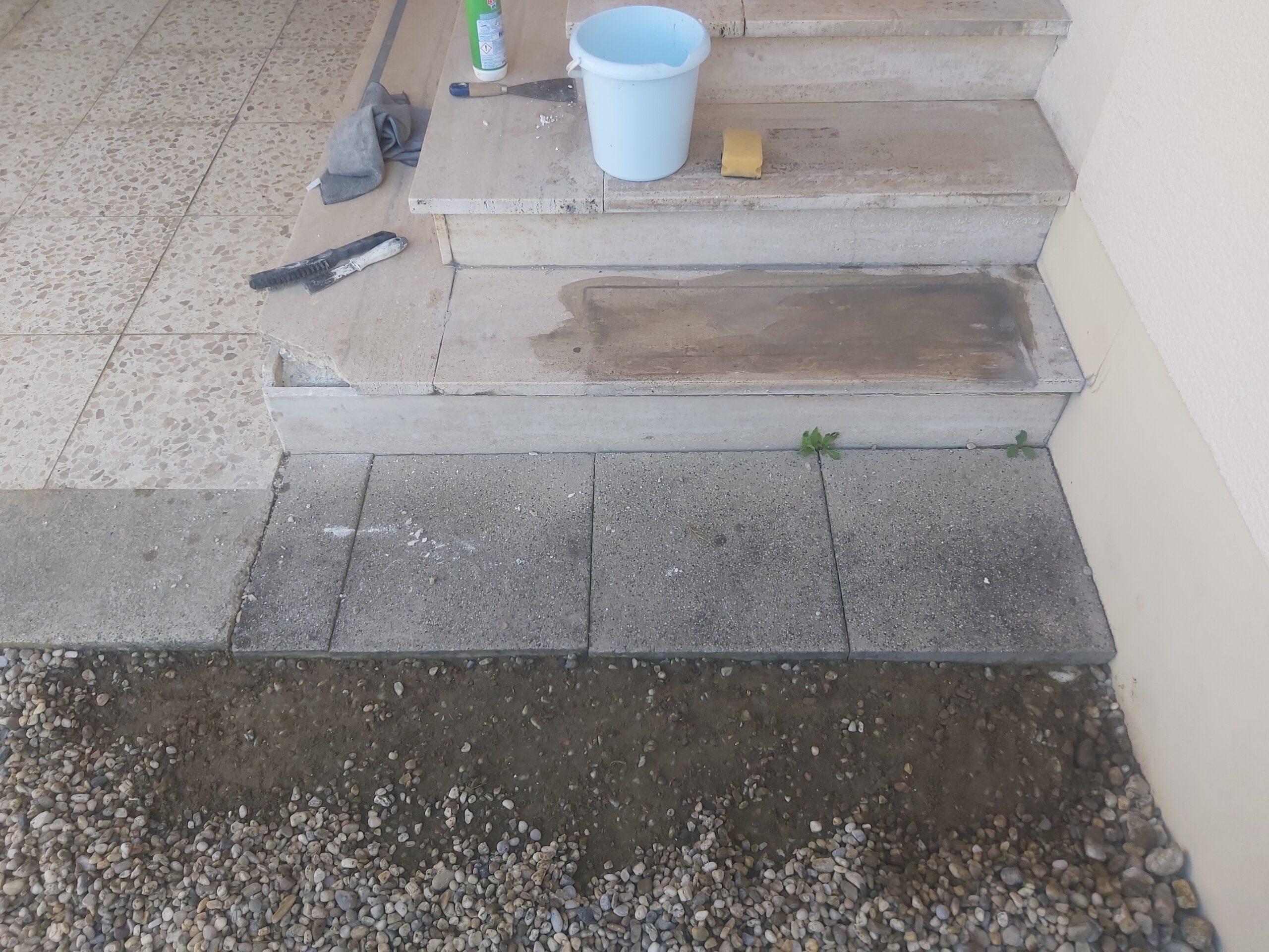 Fragment nawierzchni przed schodami wejściowymi z ułożonymi płytami betonowymi na przygotowanym podłożu, w trakcie prac wykończeniowych.