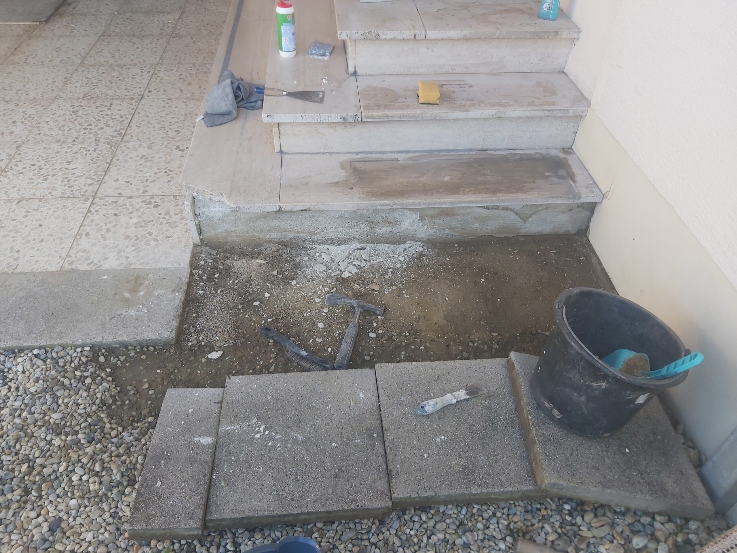 Przestrzeń przed schodami wejściowymi w trakcie prac przygotowawczych, z odsłoniętym podłożem, narzędziami oraz elementami nawierzchni przed montażem.