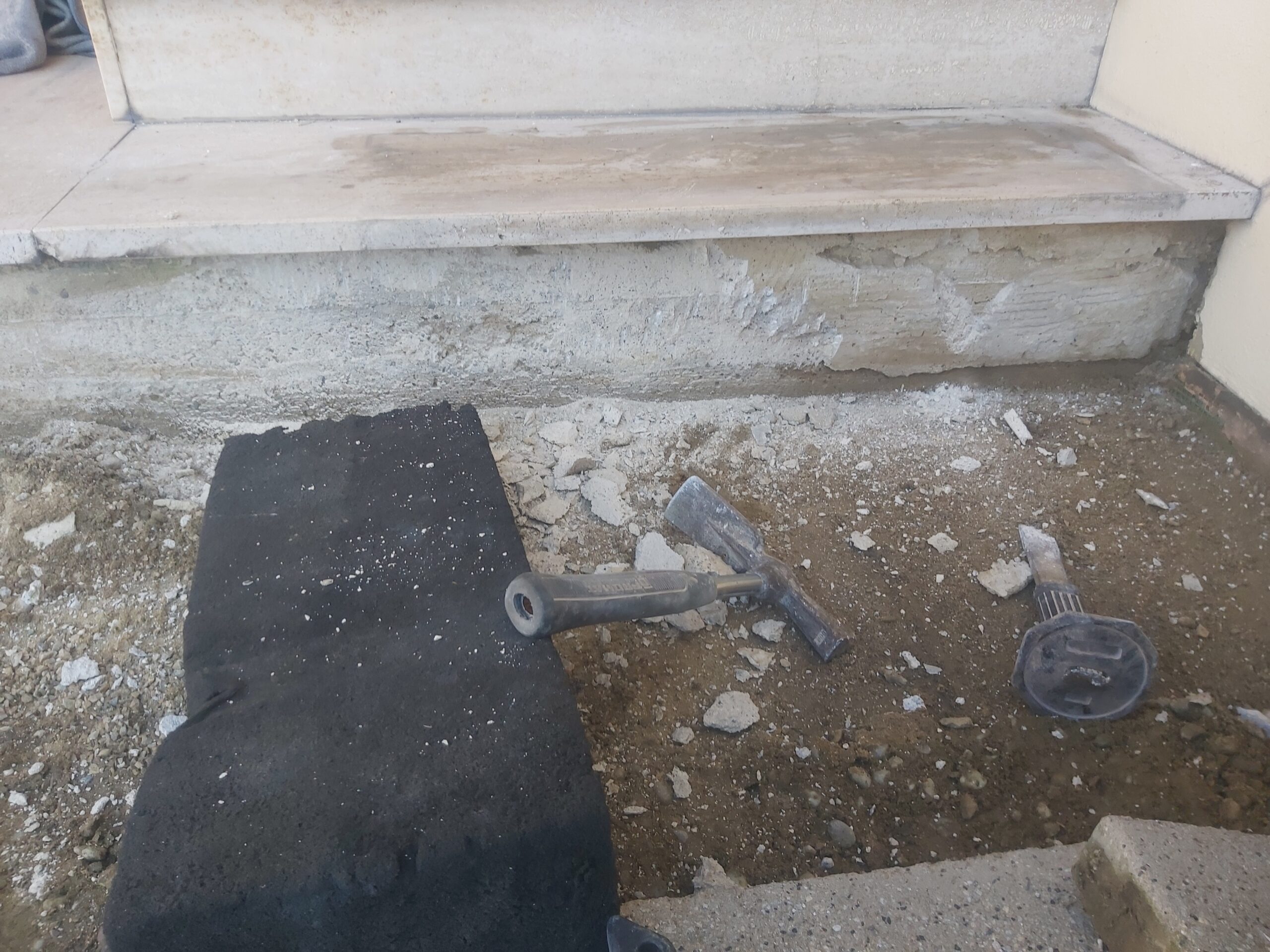 Fragment podłoża przed schodami z usuniętą warstwą betonu, widocznymi narzędziami i przygotowaniem powierzchni do dalszych prac wykończeniowych.