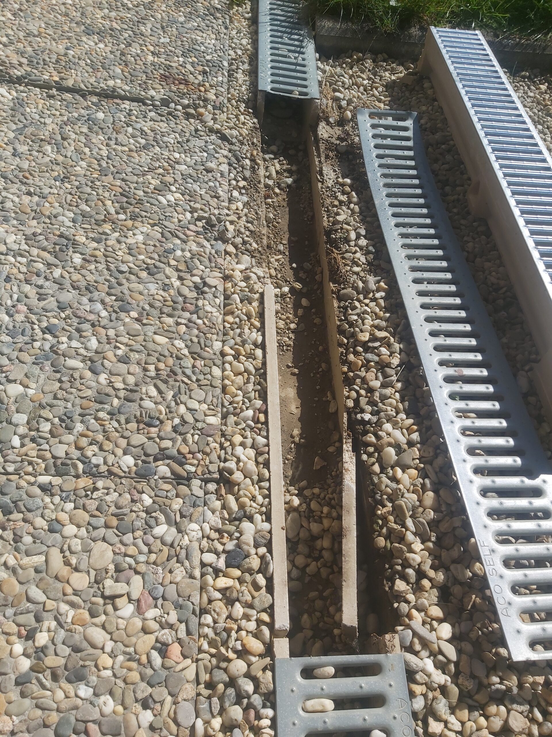 Wykopane koryto pod odwodnienie liniowe w żwirowej nawierzchni, z widocznymi elementami systemu i przygotowaniem do osadzenia korytek.