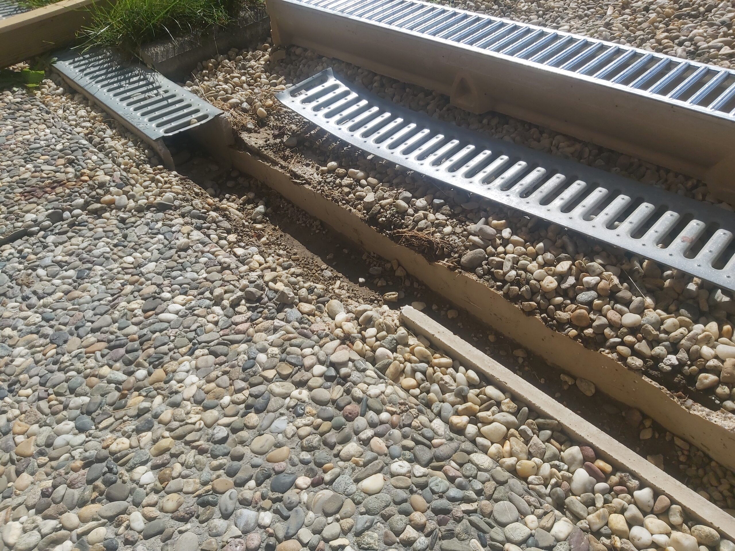 Otwarty fragment żwirowej nawierzchni z osadzanym odwodnieniem liniowym, pokazujący etap montażu korytek i przygotowanie podłoża pod stabilne osadzenie.