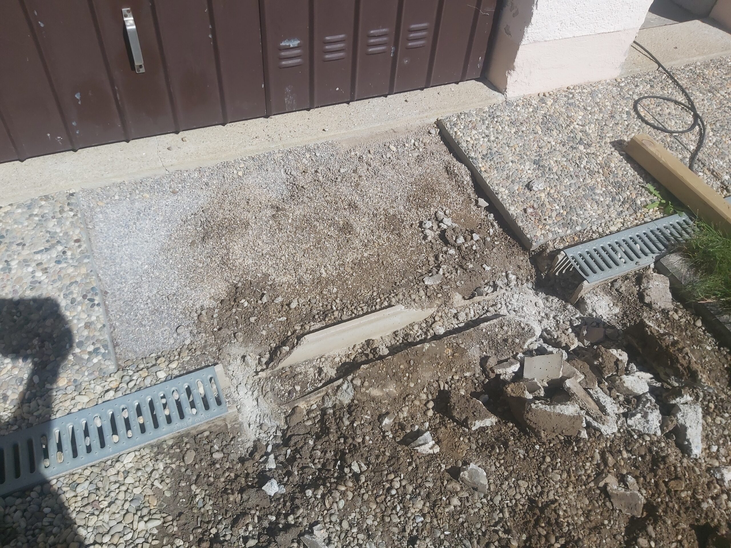 Wjazd do garażu w trakcie prac ziemnych i demontażu odwodnienia liniowego, z odsłoniętym podłożem, gruzem i elementami przygotowanymi do dalszych prac.