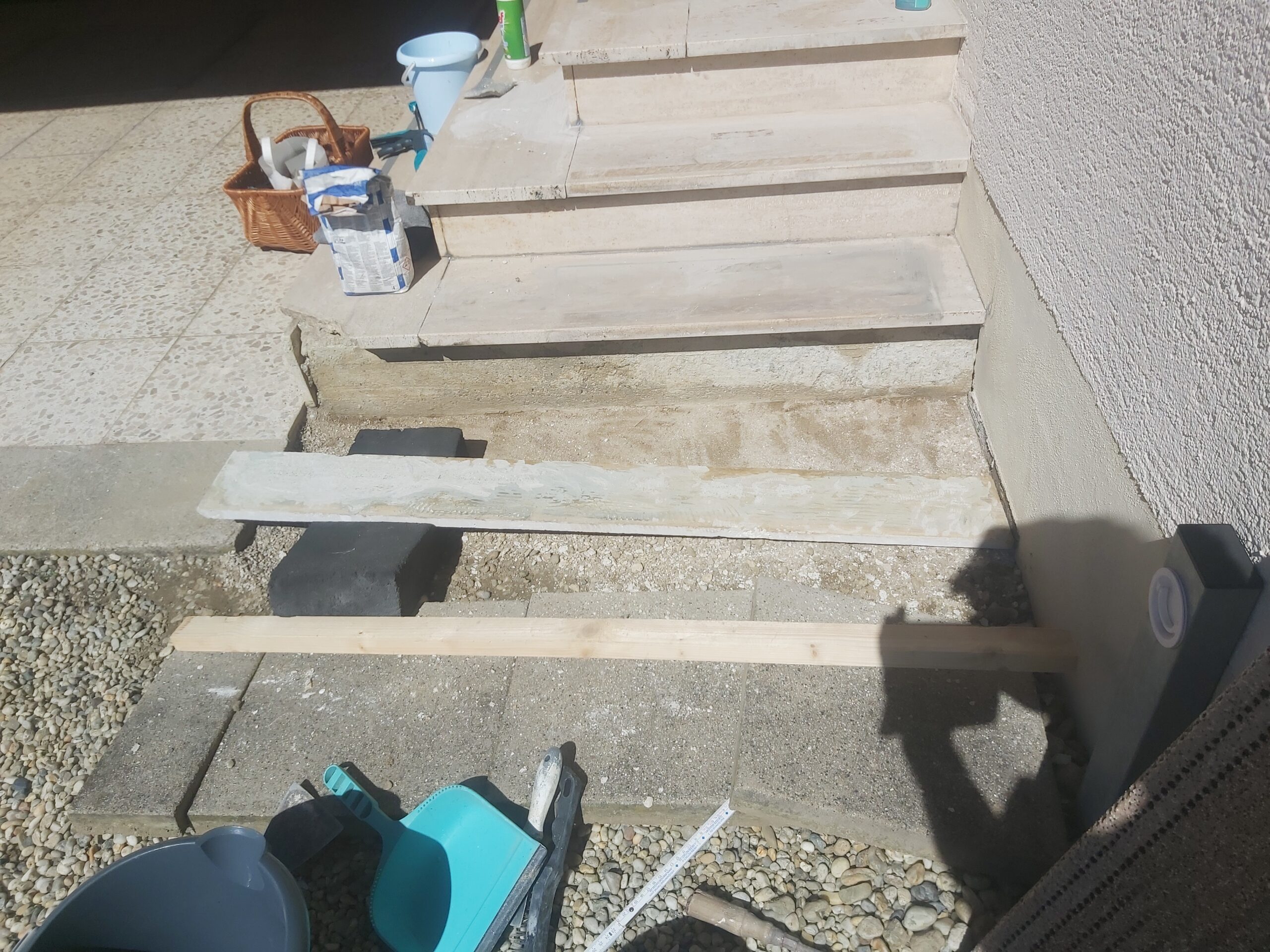 Fragment terenu przed schodami wejściowymi w trakcie wyrównywania podłoża, z użyciem listew prowadzących, narzędzi i materiałów do prac wykończeniowych.