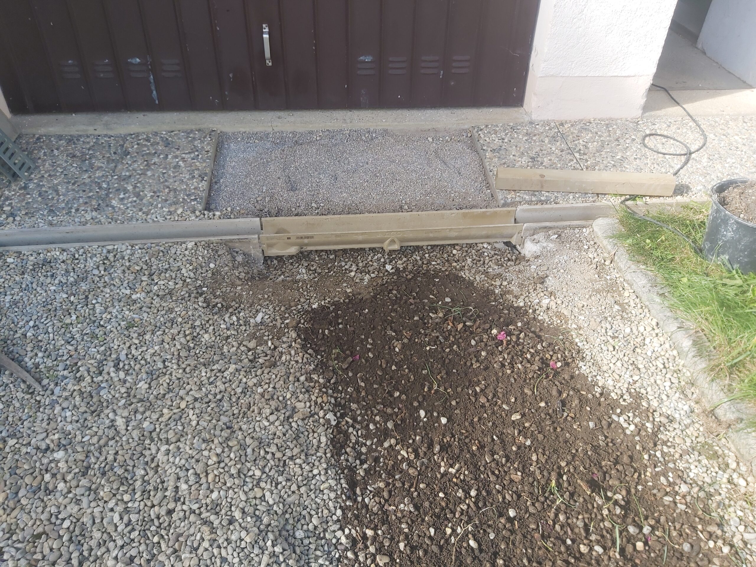 Fragment wjazdu do garażu w trakcie regulacji obrzeża i nawierzchni, z widocznym podłożem, deską dystansową i przygotowaniem do dalszych prac.