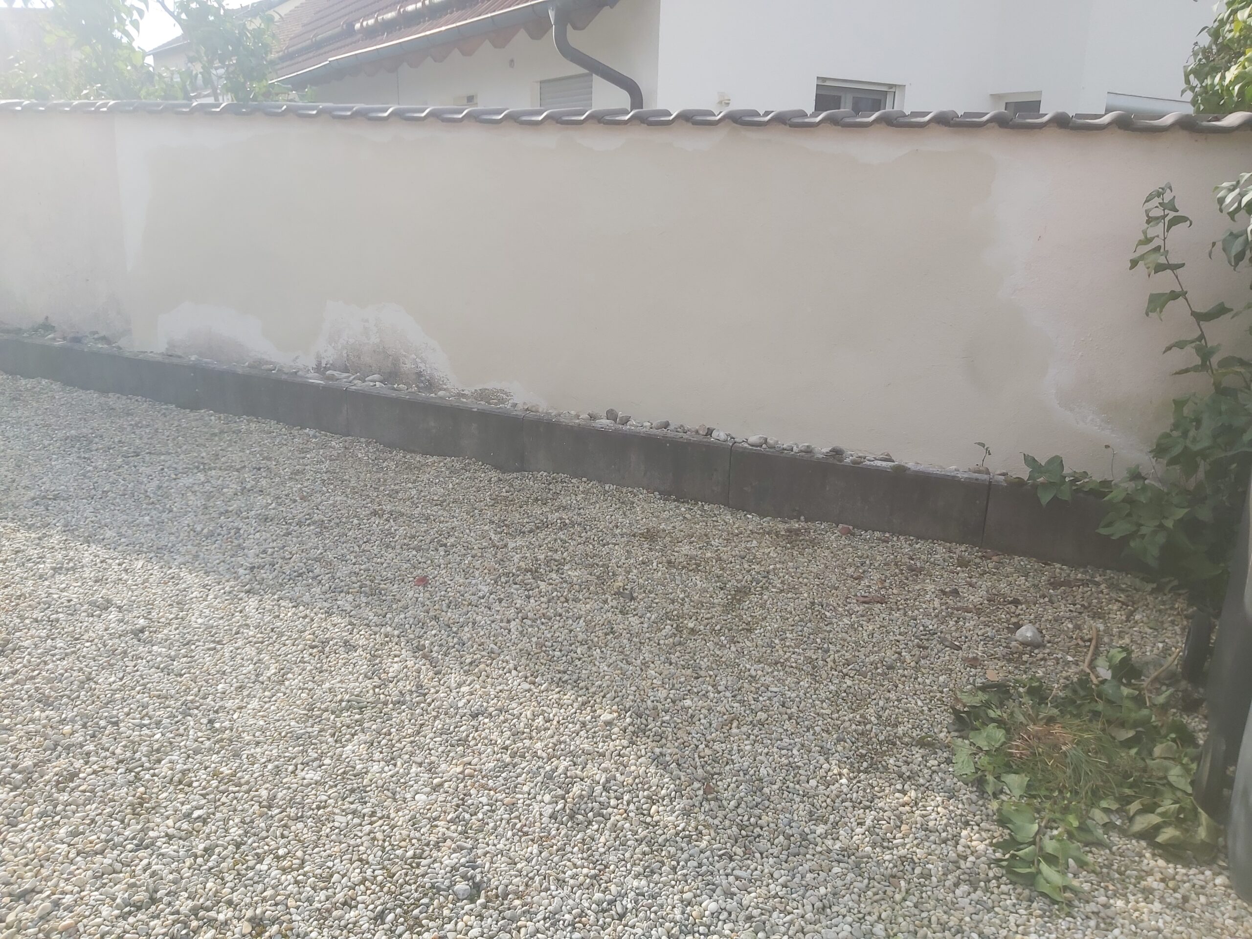 Fragment terenu z wyrównanym, żwirowym podłożem wzdłuż ogrodzenia, przygotowanym jako stabilna i estetyczna nawierzchnia wokół posesji.