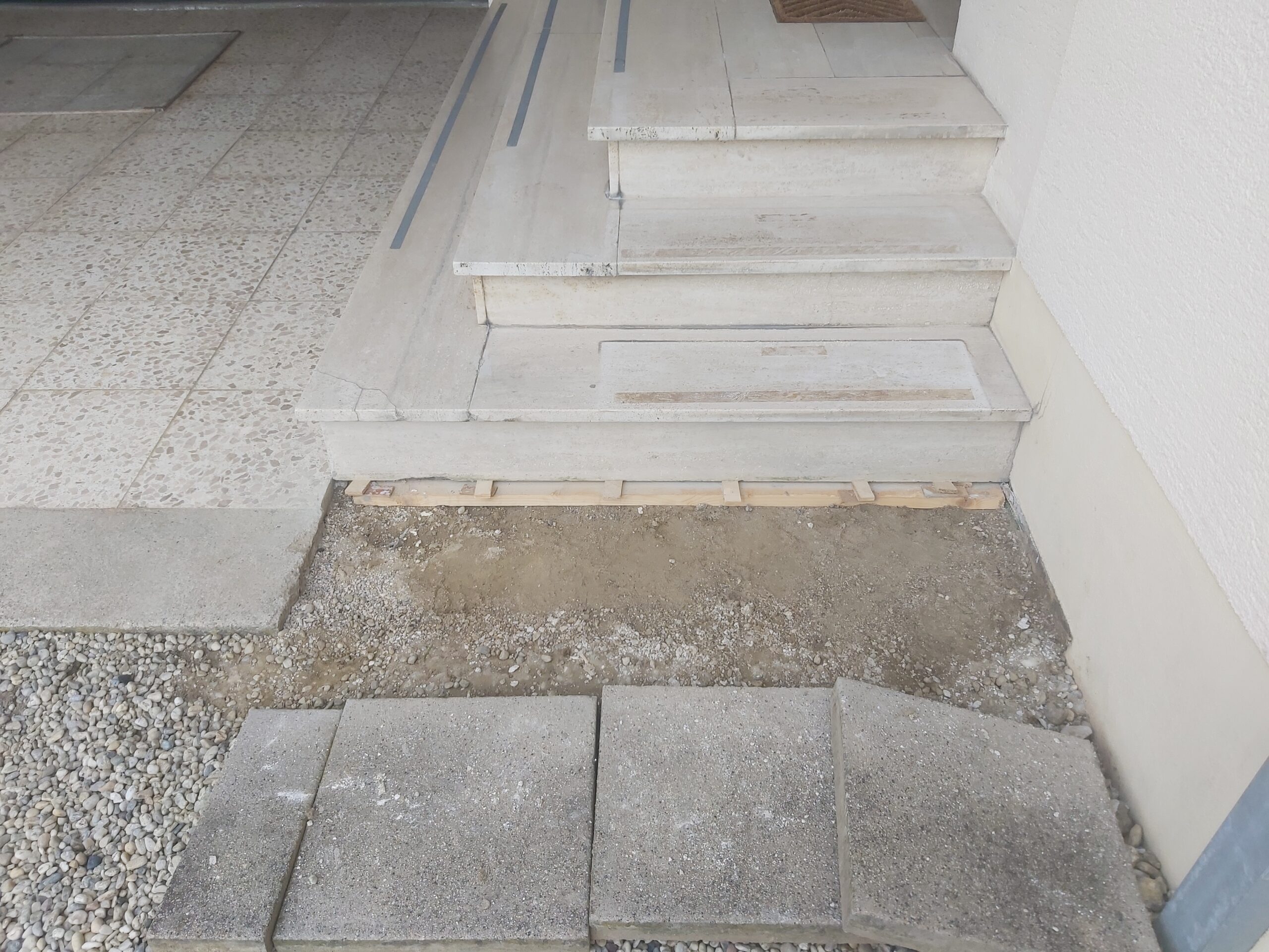 Odsłonięte podłoże przed schodami wejściowymi po usunięciu płyt nawierzchniowych, przygotowane do dalszych prac brukarskich.