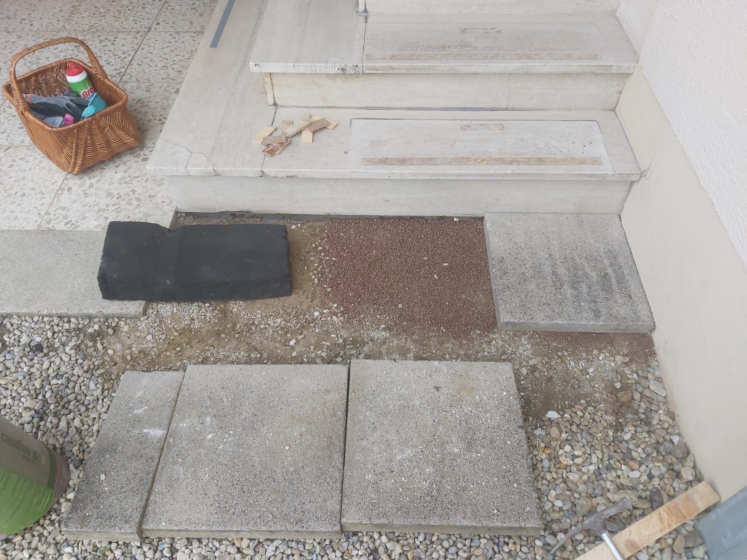 Fragment terenu przed schodami wejściowymi w trakcie przygotowania podłoża, z widoczną podsypką, płytami betonowymi i elementami nawierzchni przed ułożeniem.
