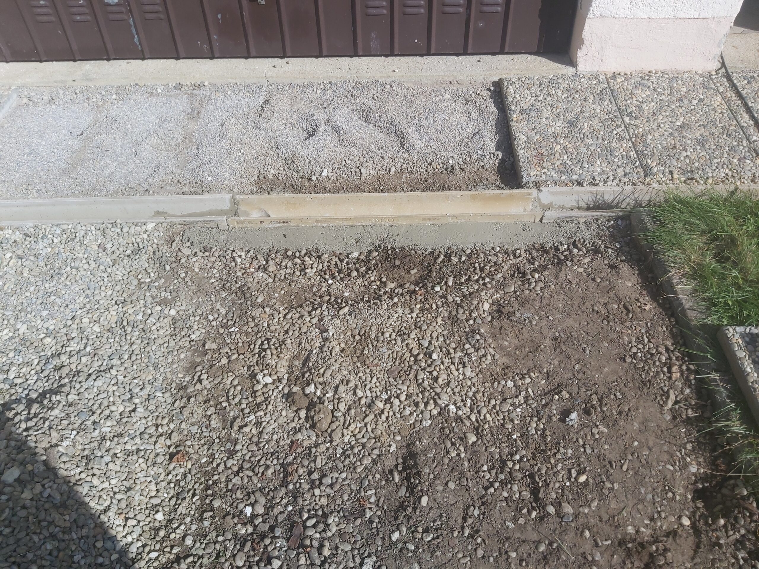 Fragment wjazdu do garażu w trakcie prac, z odsłoniętym podłożem, obrzeżem betonowym i przygotowaniem nawierzchni do dalszego utwardzania.