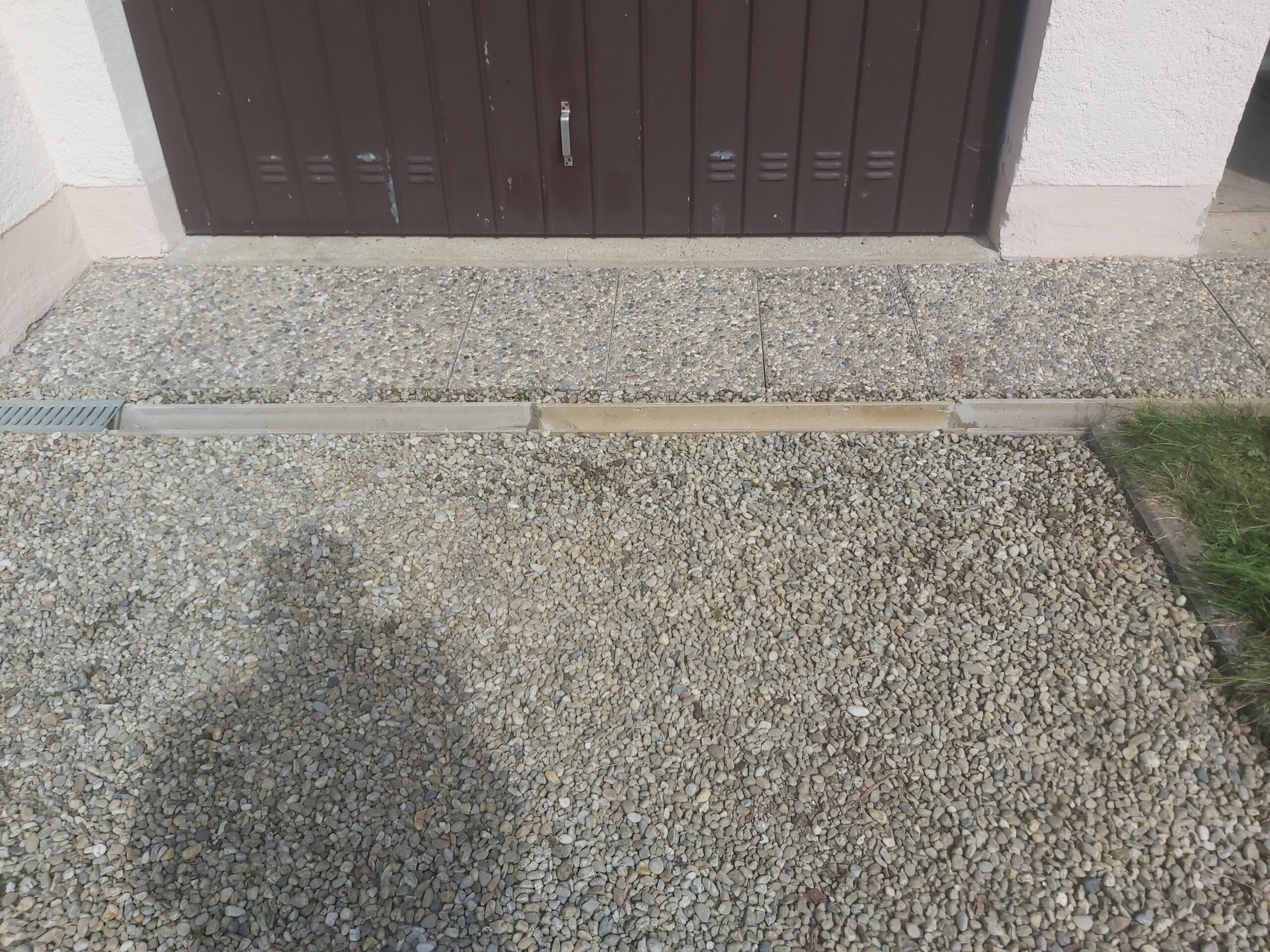 Utwardzona nawierzchnia żwirowa przed garażem z widocznym odwodnieniem liniowym i estetycznym połączeniem z elewacją budynku.