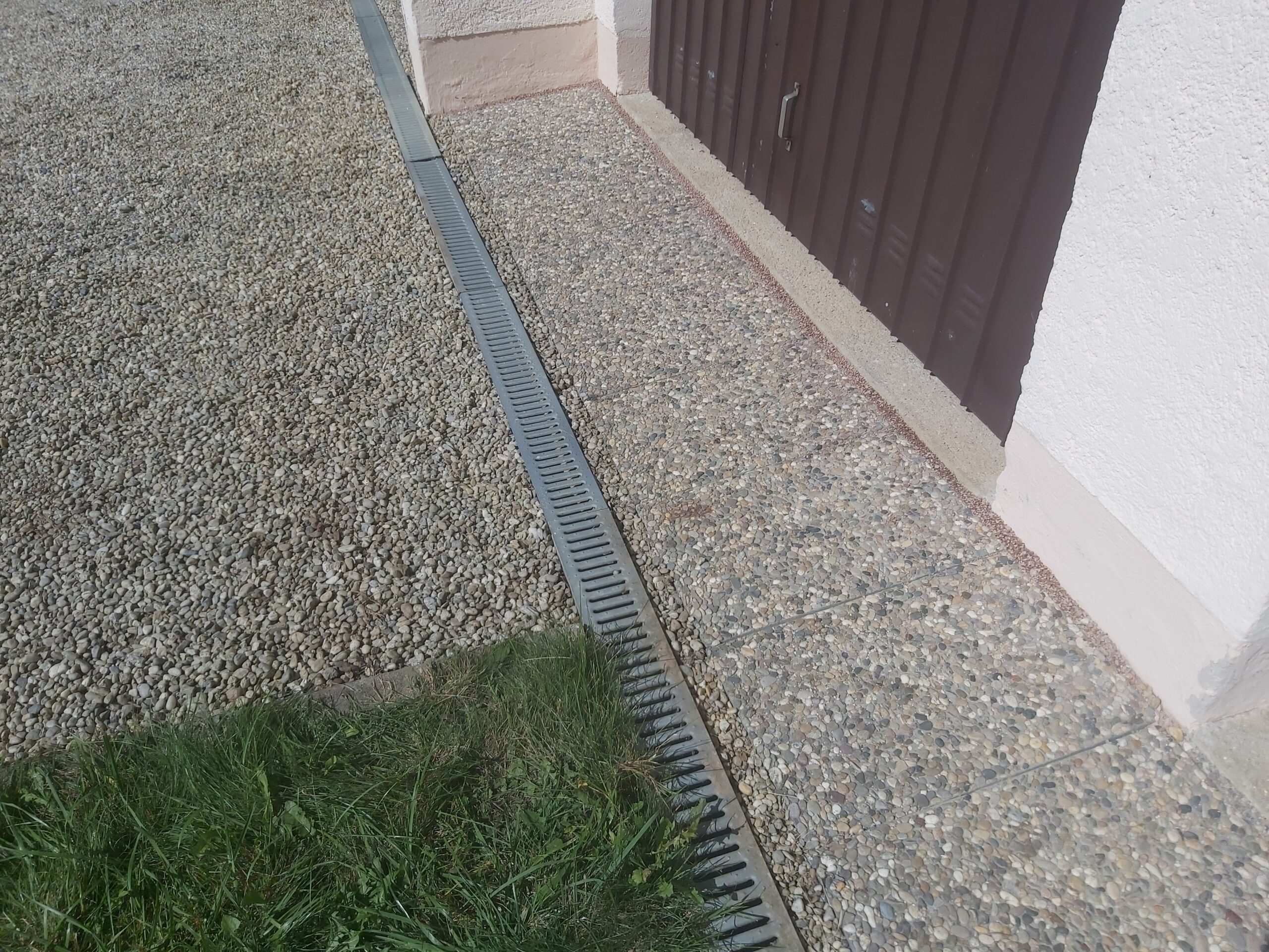 Zbliżenie na odwodnienie liniowe zamontowane w żwirowej nawierzchni przed garażem, zapewniające skuteczne odprowadzanie wody opadowej.