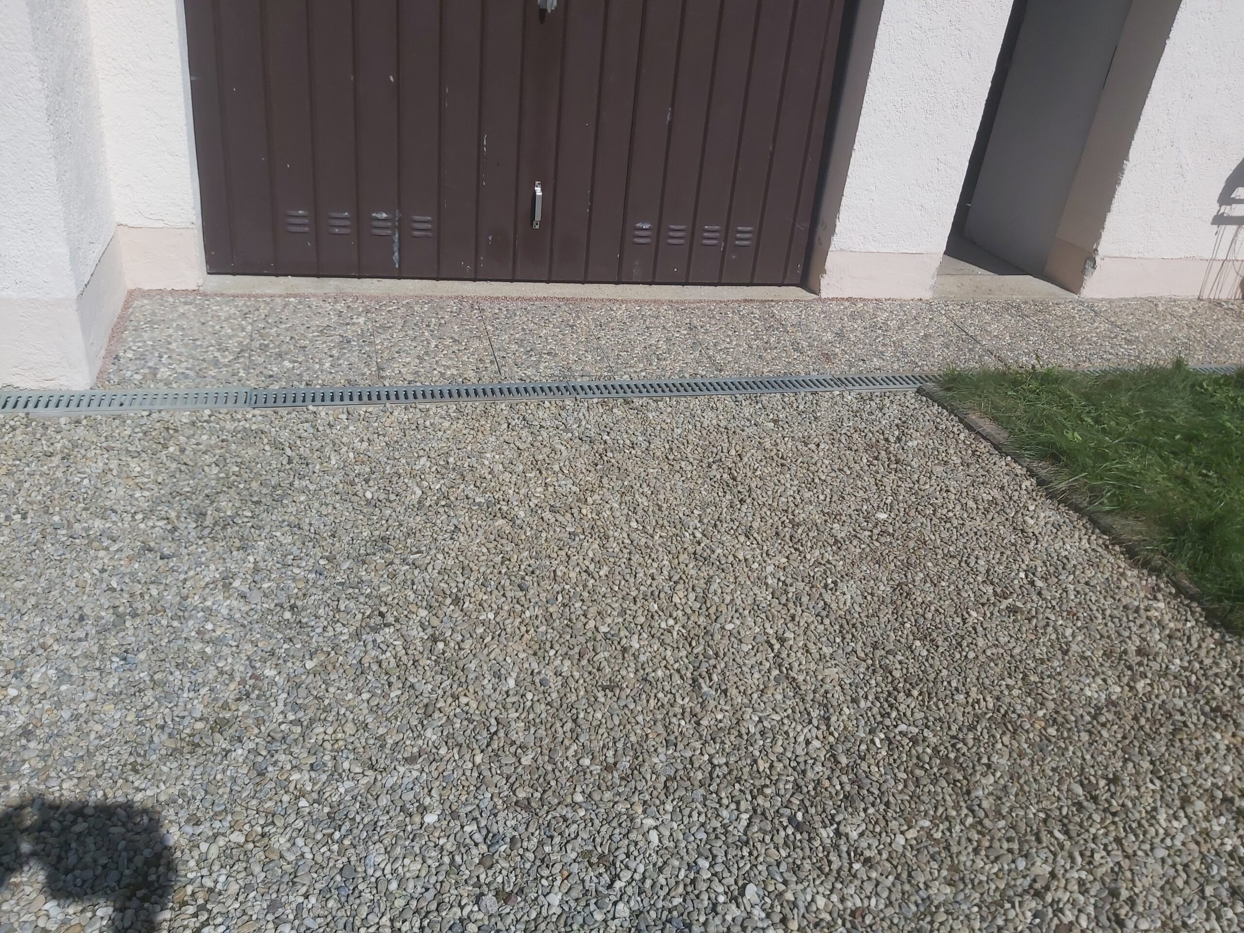 Utwardzona nawierzchnia z drobnego żwiru przed bramą garażową, z widocznym odwodnieniem liniowym i estetycznym połączeniem z trawnikiem.