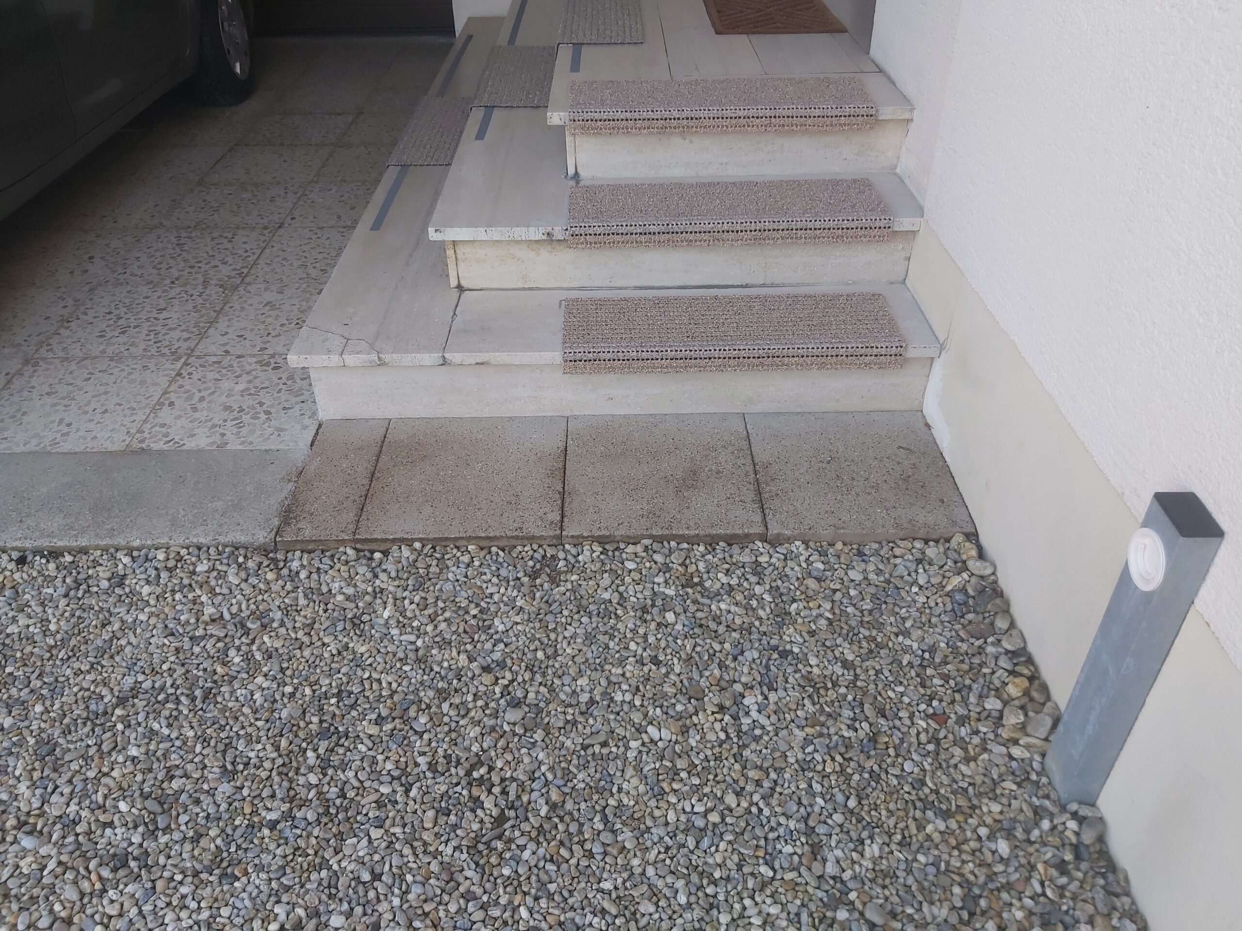 Schody wejściowe z jasnego kamienia połączone z żwirową nawierzchnią, tworzące estetyczne i funkcjonalne przejście przy elewacji budynku.