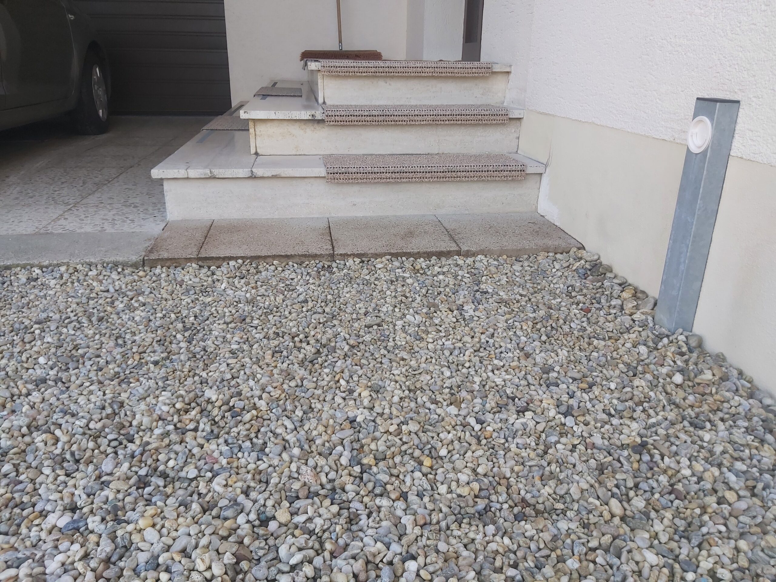 Utwardzona nawierzchnia z drobnego żwiru przed schodami wejściowymi, estetycznie połączona z betonowymi stopniami i elewacją budynku.