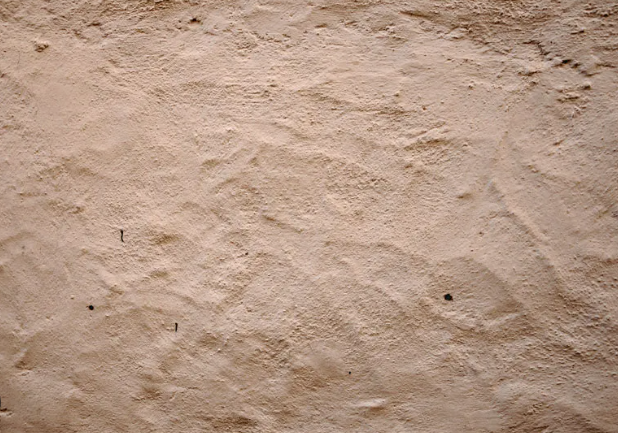 Zbliżenie na chropowatą, nierówną strukturę jasnego tynku na ścianie.