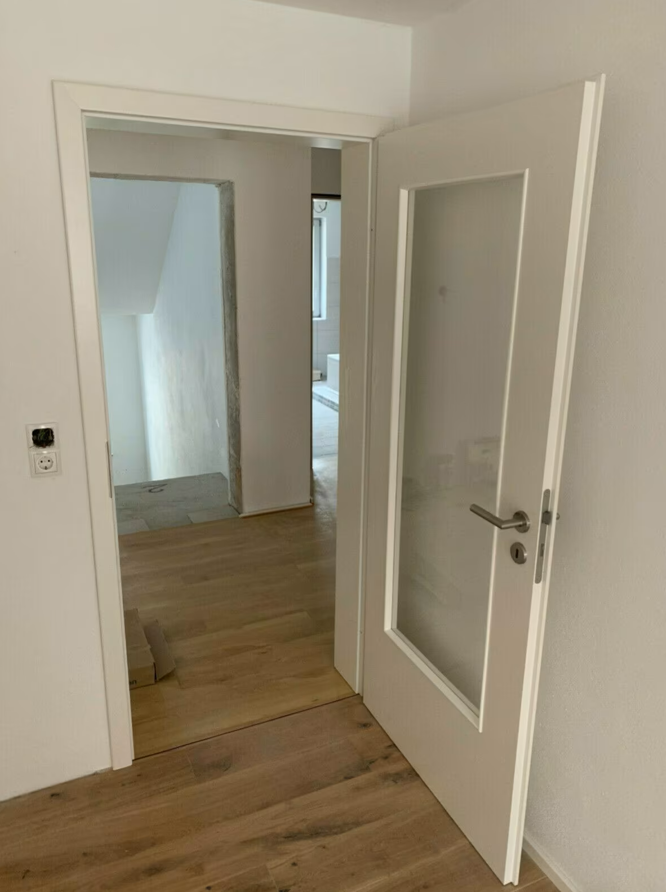 Zamontowane białe drzwi wewnętrzne z przeszkleniem, otwarte na korytarz z drewnianą podłogą, prezentujące efekt końcowy po pracach wykończeniowych.