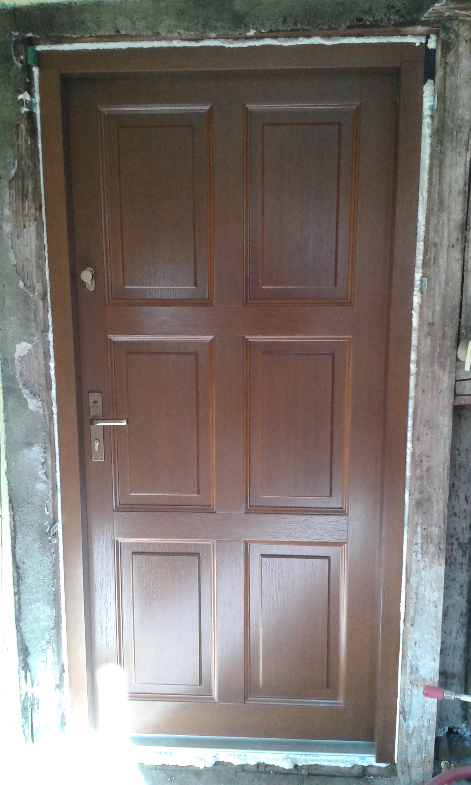 Drzwi wejściowe zamontowane w otworze z widoczną pianką montażową i nieukończonym ościeżem, przygotowane do dalszych prac wykończeniowych.