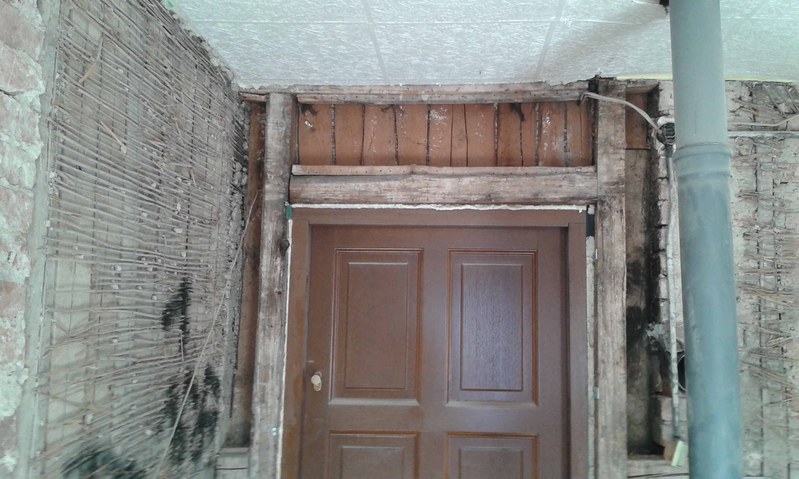 Ościeże drzwi wejściowych z odsłoniętą konstrukcją i elementami ściany, pokazujące zakres prac remontowych przed wykonaniem nowego wykończenia.