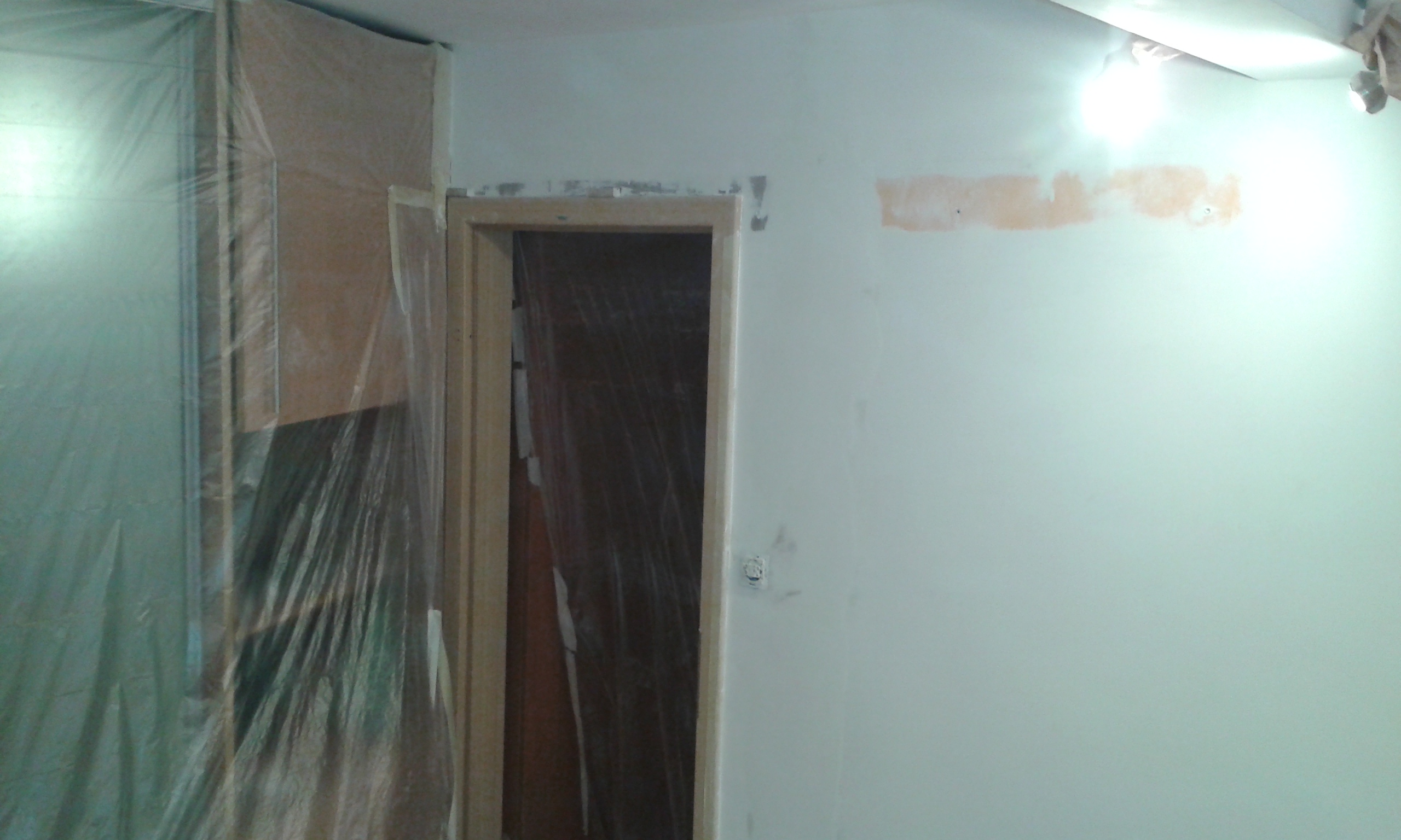 Ściana wewnętrzna z otworem drzwiowym zabezpieczonym folią oraz śladami po wcześniejszych pracach remontowych