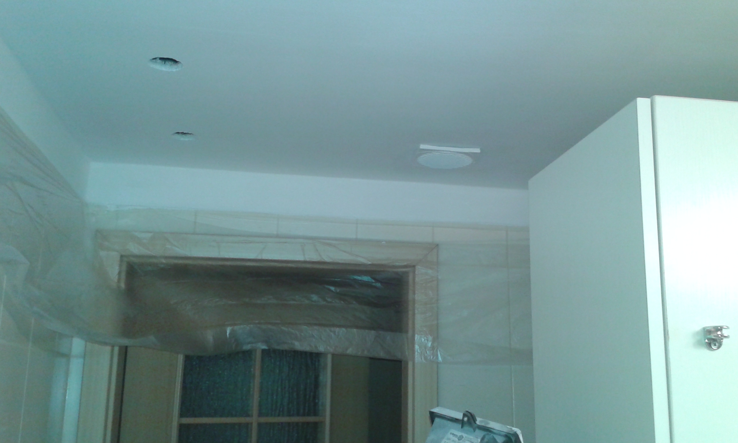 Sufit w łazience z zamontowanymi oprawami oświetleniowymi i otworem drzwiowym zabezpieczonym folią