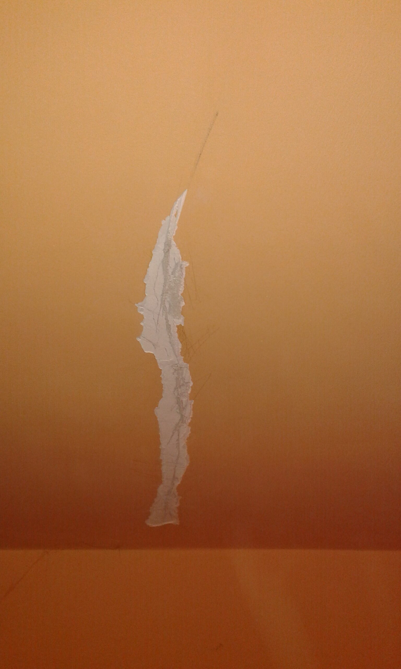 Pionowe pęknięcie farby i gładzi na pomarańczowej ścianie