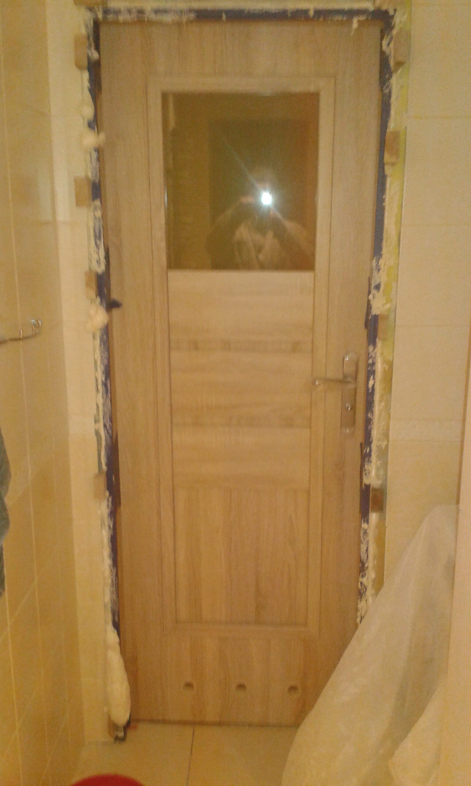 Nowo zamontowane drzwi łazienkowe z widoczną pianką montażową wokół ościeżnicy, przed wykonaniem finalnych prac wykończeniowych.