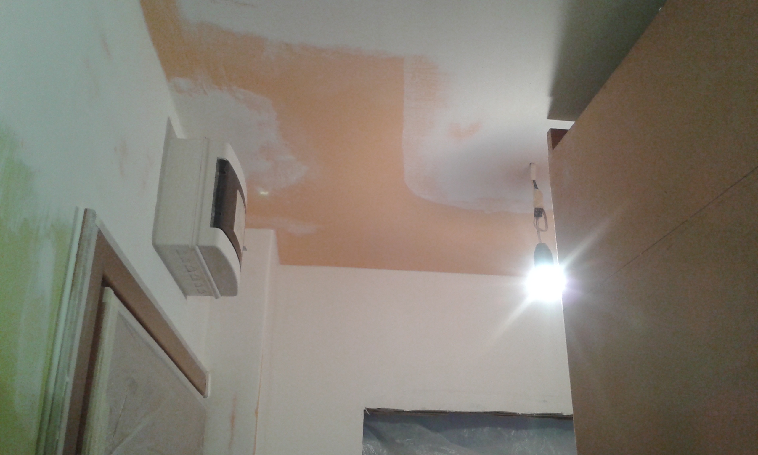 Sufit i ściana w trakcie prac wykończeniowych z widocznymi łatami szpachli i oświetleniem roboczym