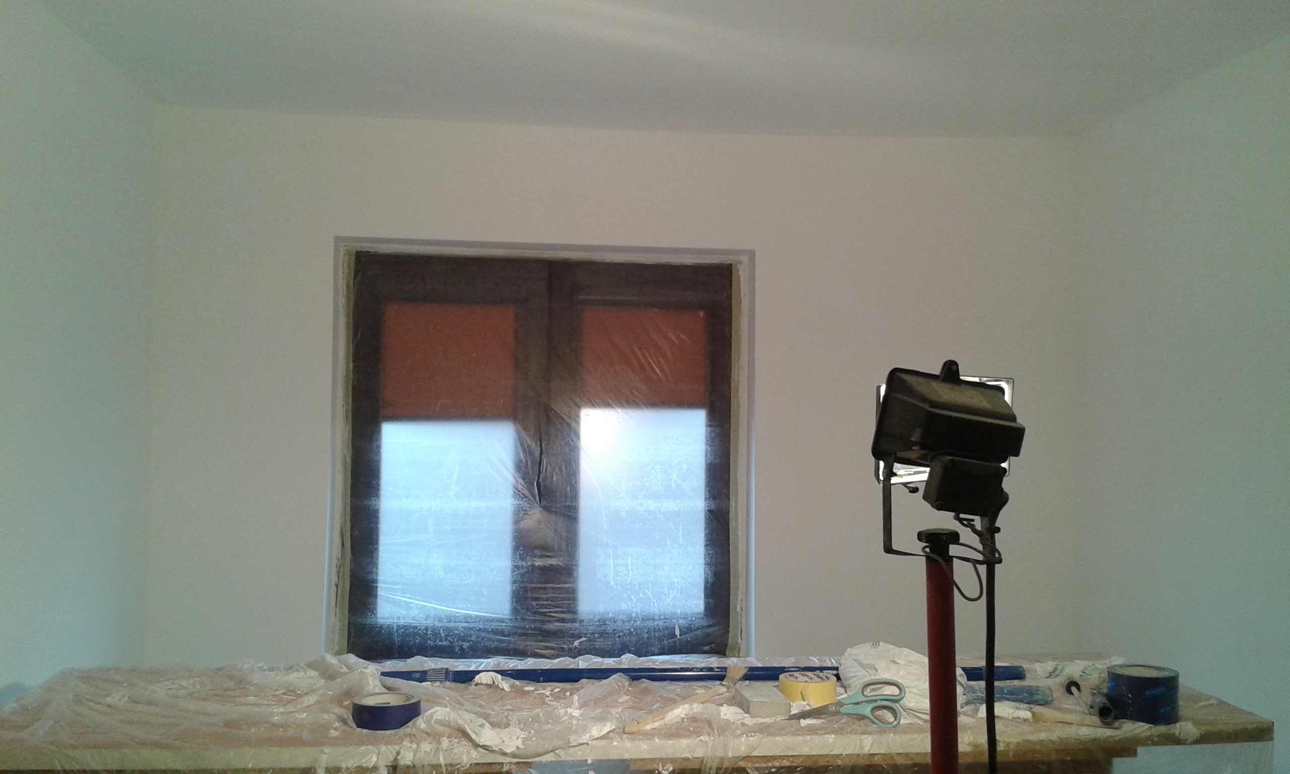 Pomieszczenie po malowaniu z zabezpieczonym oknem i stanowiskiem roboczym