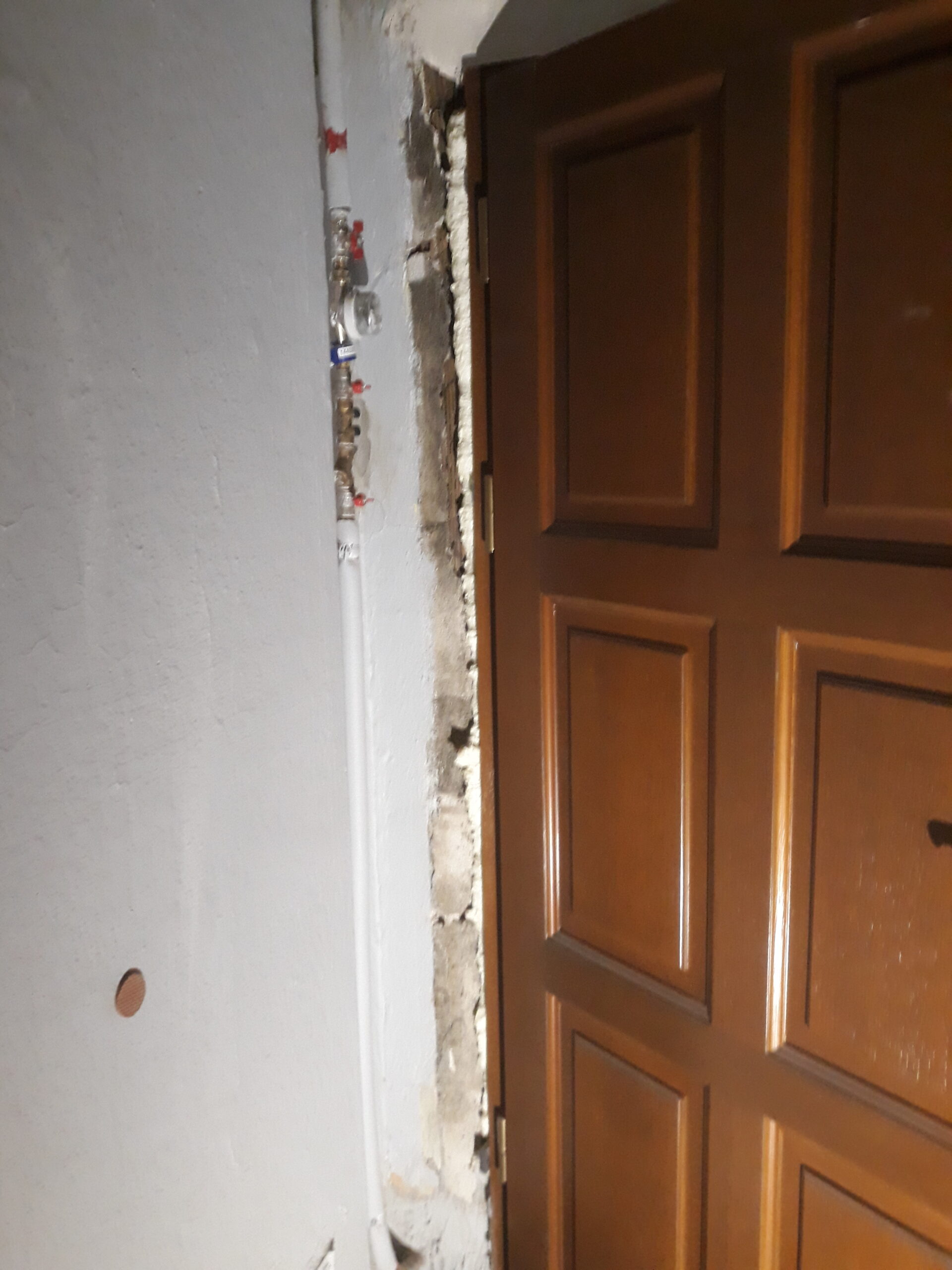 Fragment ościeżnicy drzwi wejściowych z odsłoniętą konstrukcją ściany i instalacją, pokazujący zakres prac przygotowawczych przed wykończeniem.