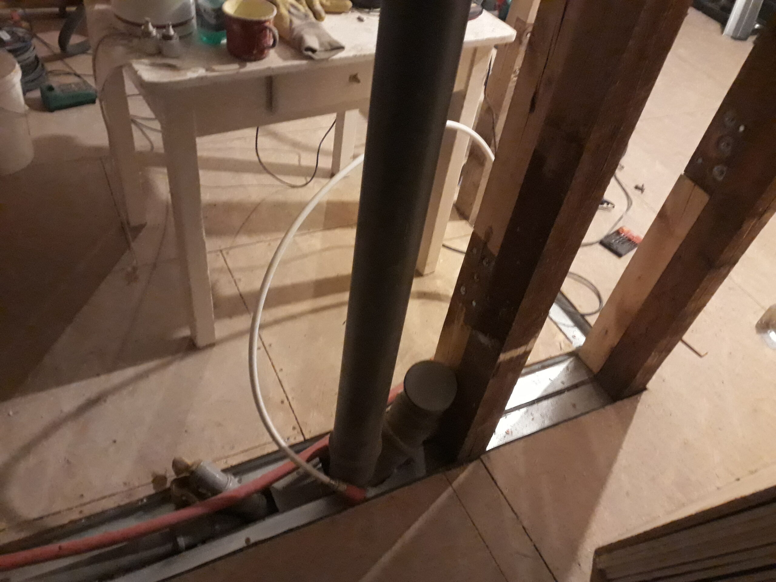 Remont poddasza – zbliżenie na fragment podłogi z widoczną rurą kanalizacyjną, przewodami instalacyjnymi oraz drewnianą konstrukcją ściany w trakcie prac budowlanych.