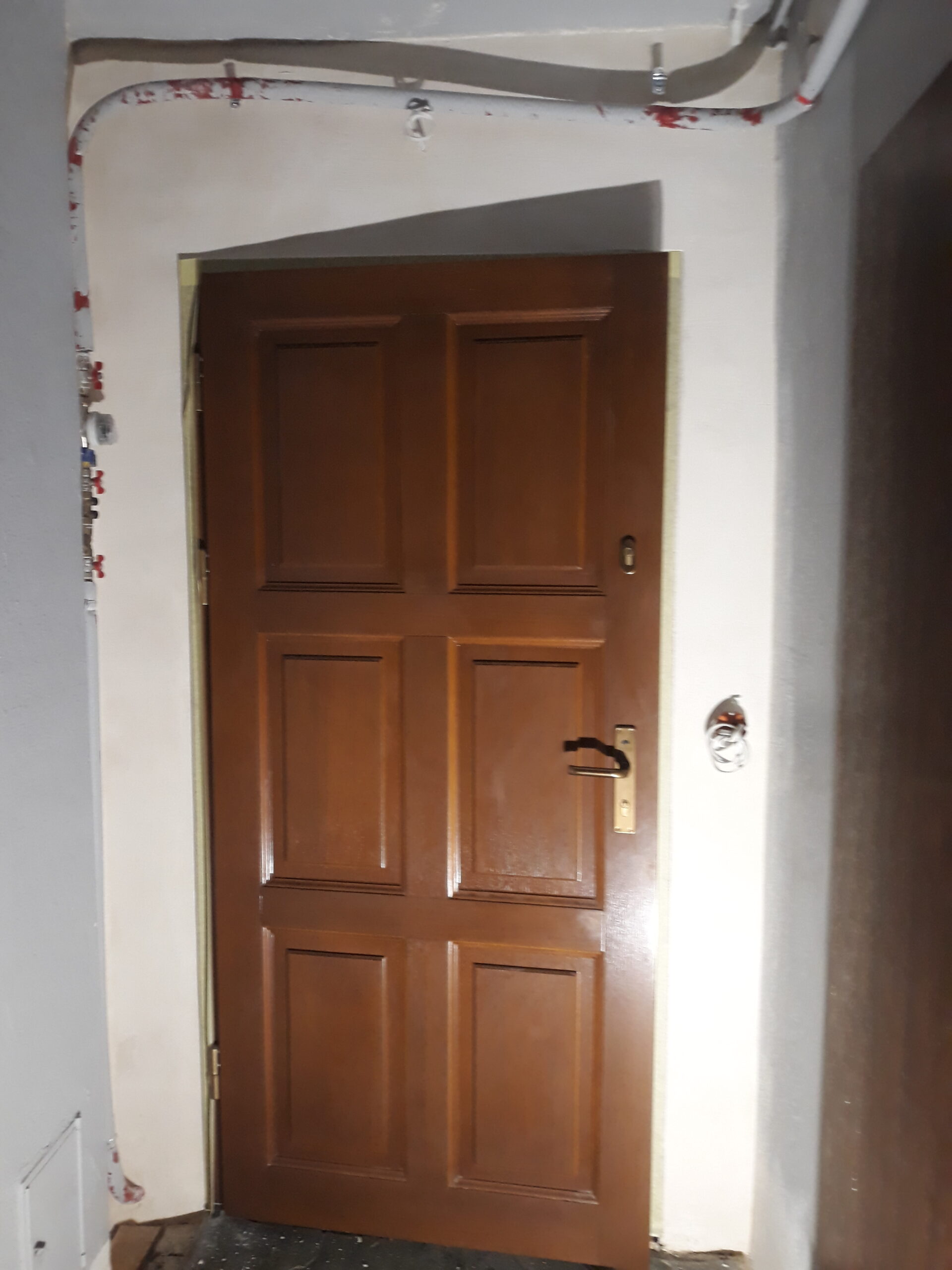 Drzwi wejściowe w trakcie prac przygotowawczych, z widocznymi bruzdami instalacyjnymi i nieukończonym wykończeniem ścian wokół ościeżnicy.